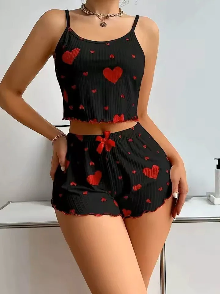 A woman is wearing a black pajama set with red hearts and a red bow on the shorts, standing against a white background.