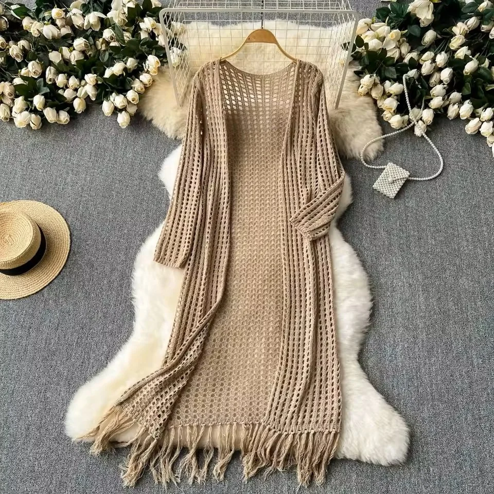 A beige crochet dress laid out on a white faux fur rug, surrounded by white roses, a straw hat, and a pearl purse, with a white wire rack in the background.