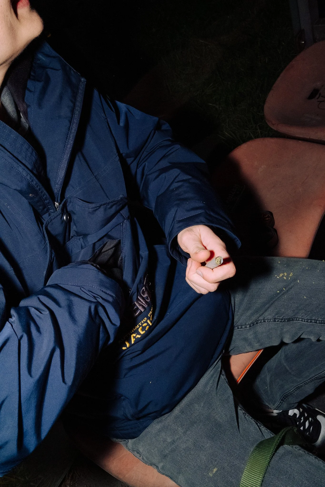 Person in blauer Jacke hält eine Zigarettenkippe und sitzt auf einem Stuhl.