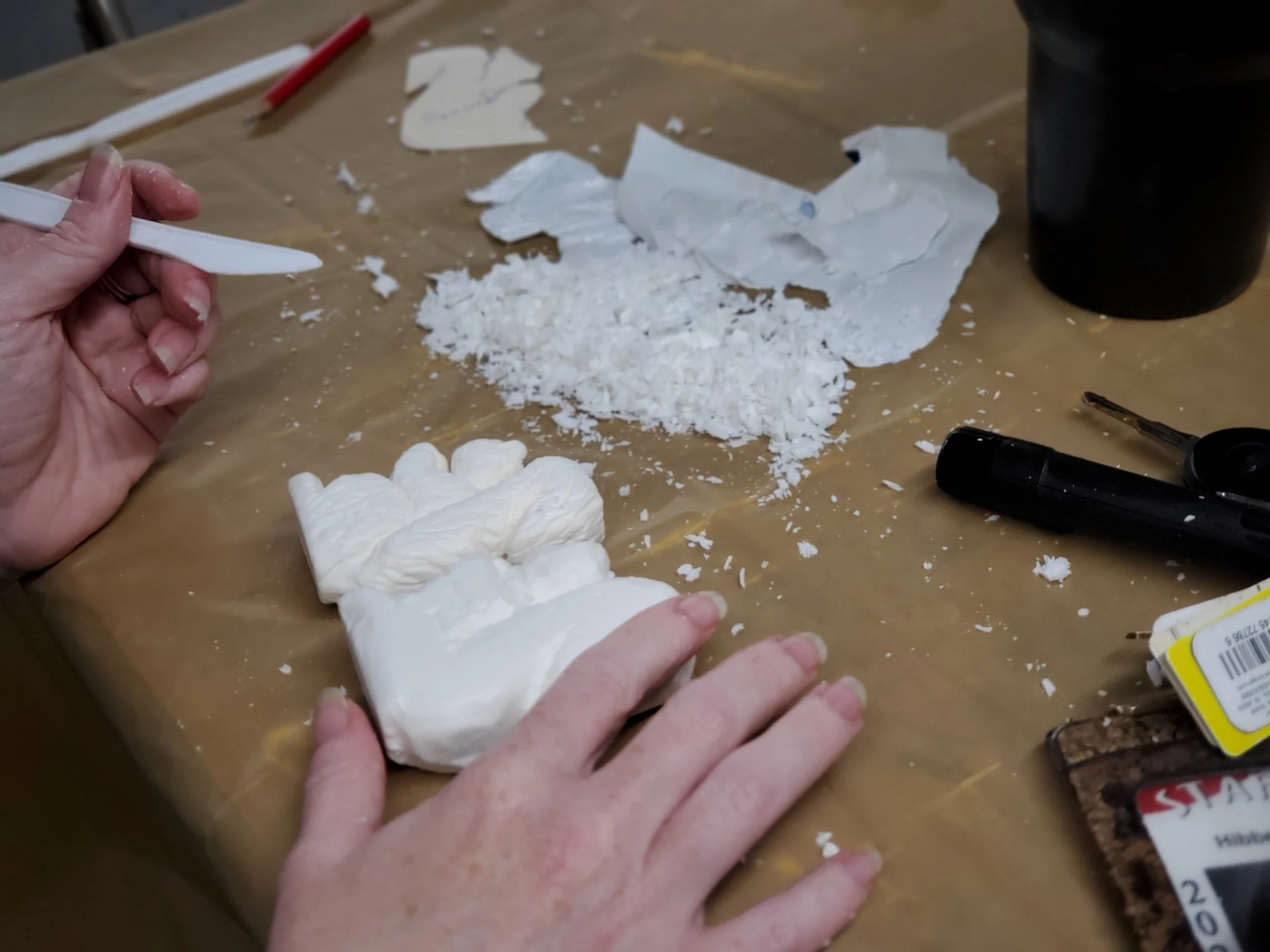 Person handling white powdery substance on a table, with broken pieces and tools nearby.