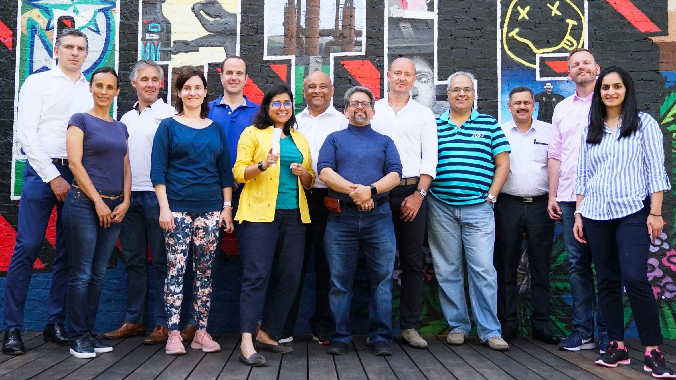 Group of diverse people standing together outdoors in front of a colorful graffiti wall, smiling at the camera.
