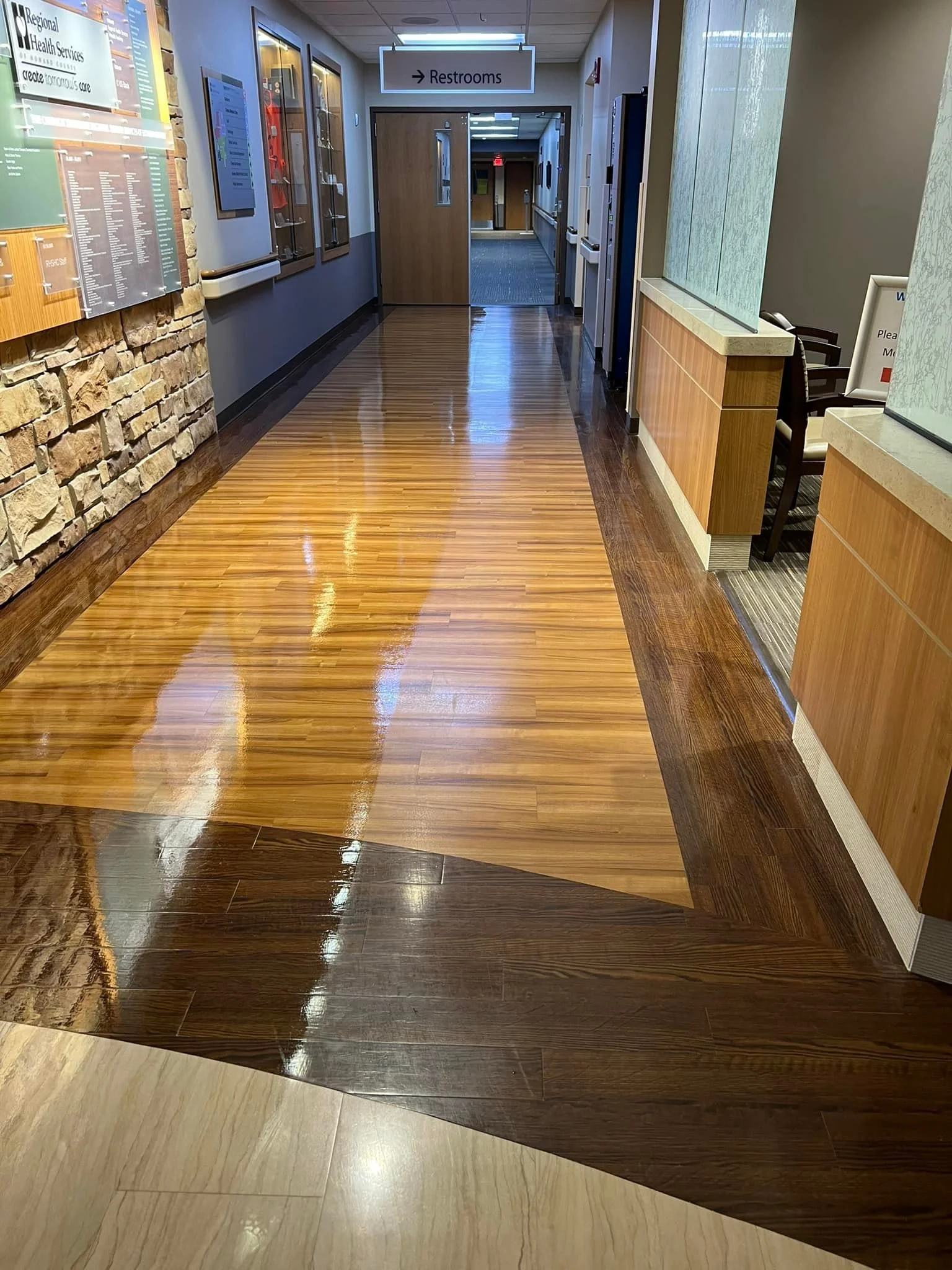 Polished wooden hallway floor in a building, with a sign indicating restrooms ahead.