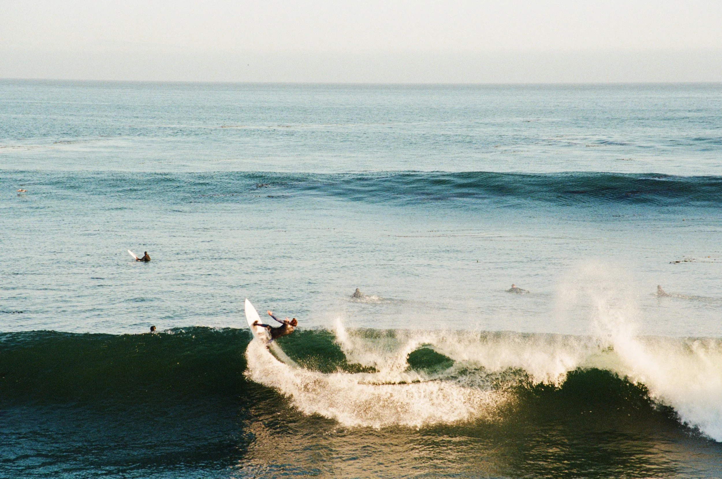 Surfer riding a wave in the ocean with other surfers in the background.