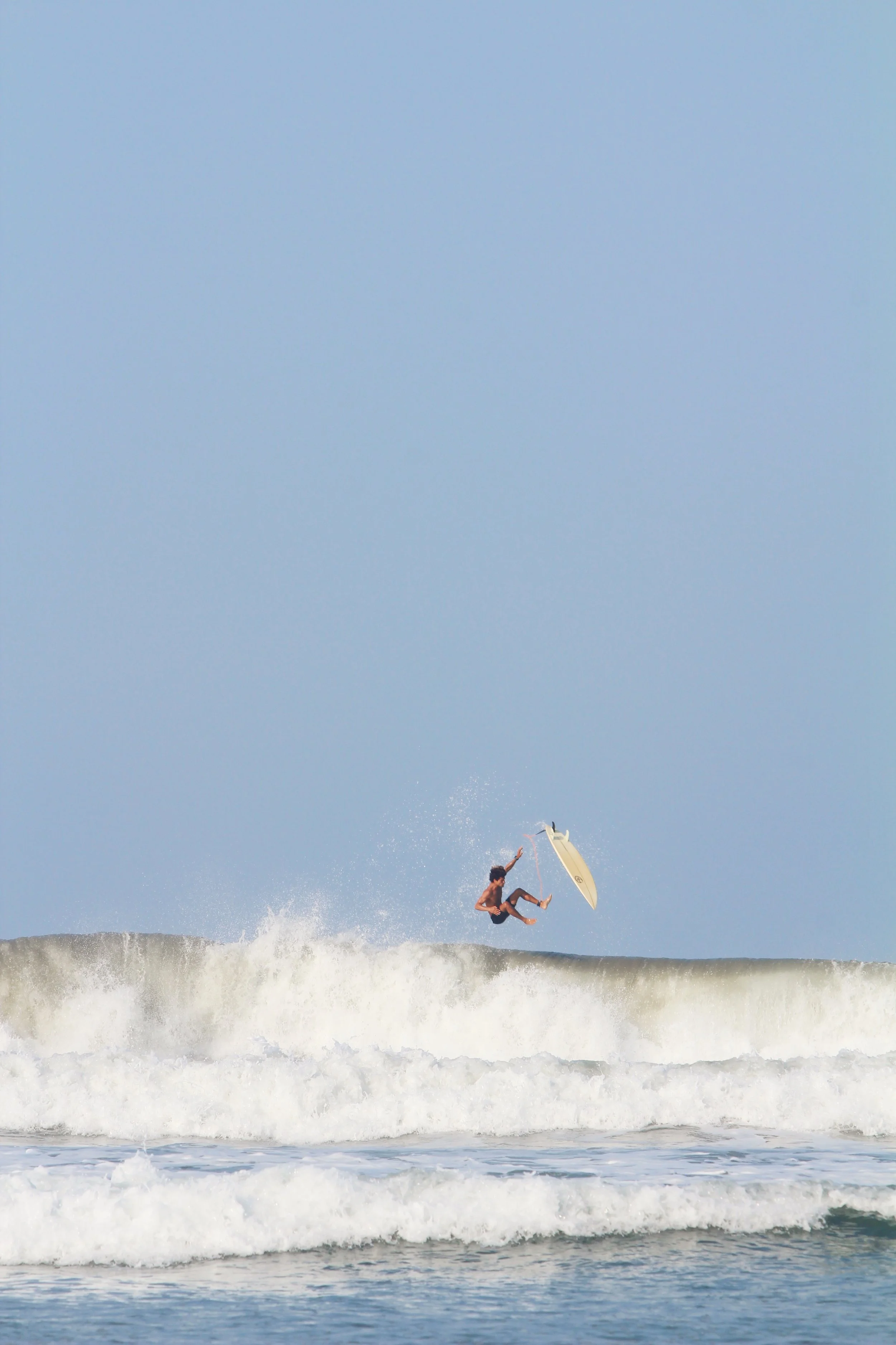 A person surfing and performing an aerial trick on a wave in the ocean under a clear sky.