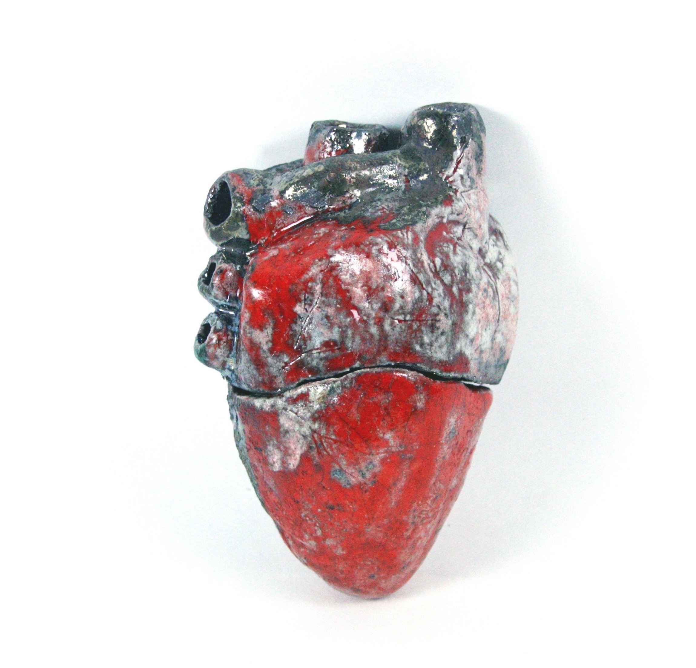 Close-up image of a sculpture with a rough, uneven surface, painted red and black, against a white background.