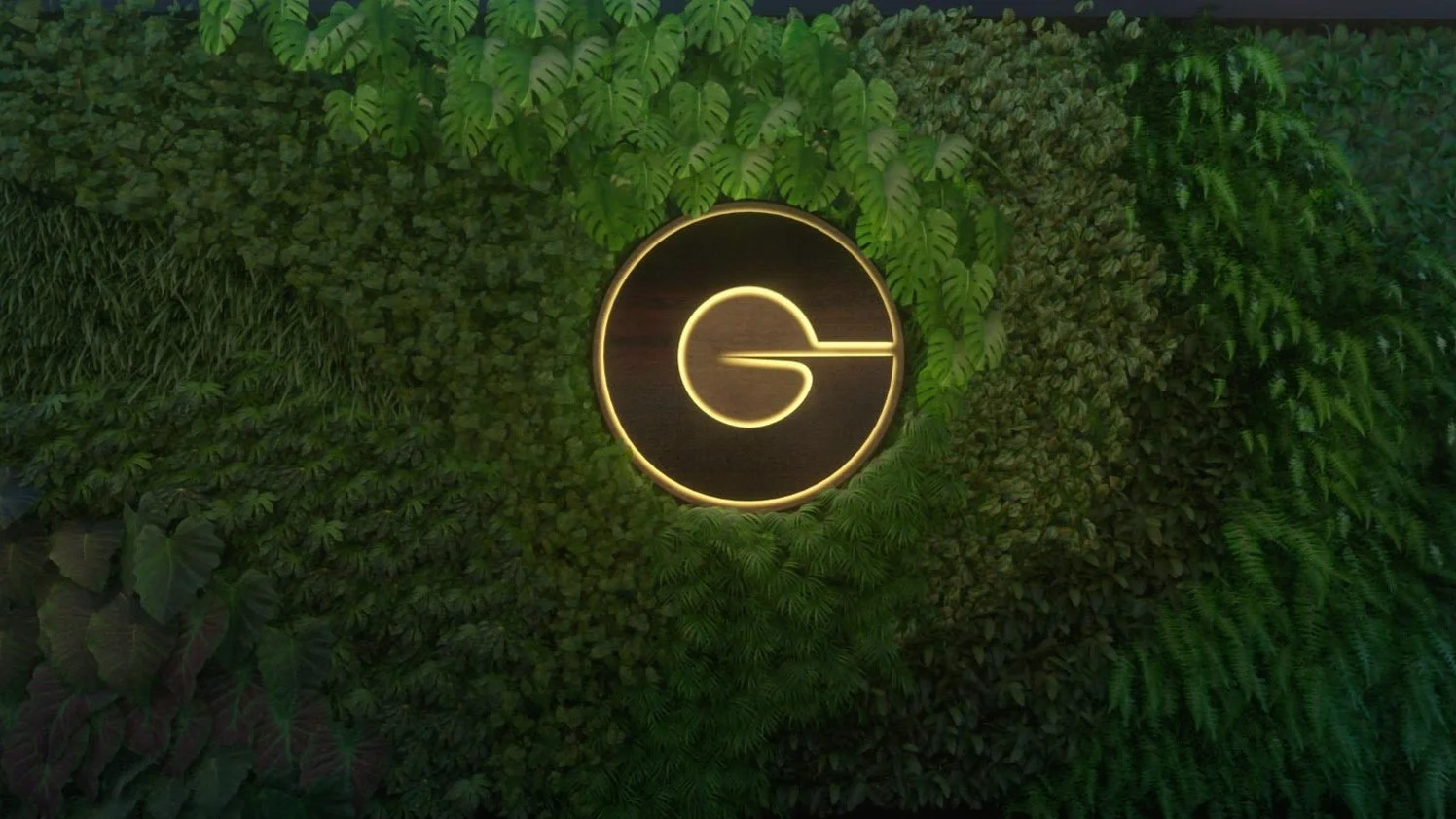 A decorative wall with green foliage and a glowing circular logo featuring the letter 'G' in the center, illuminated with warm yellow lighting.