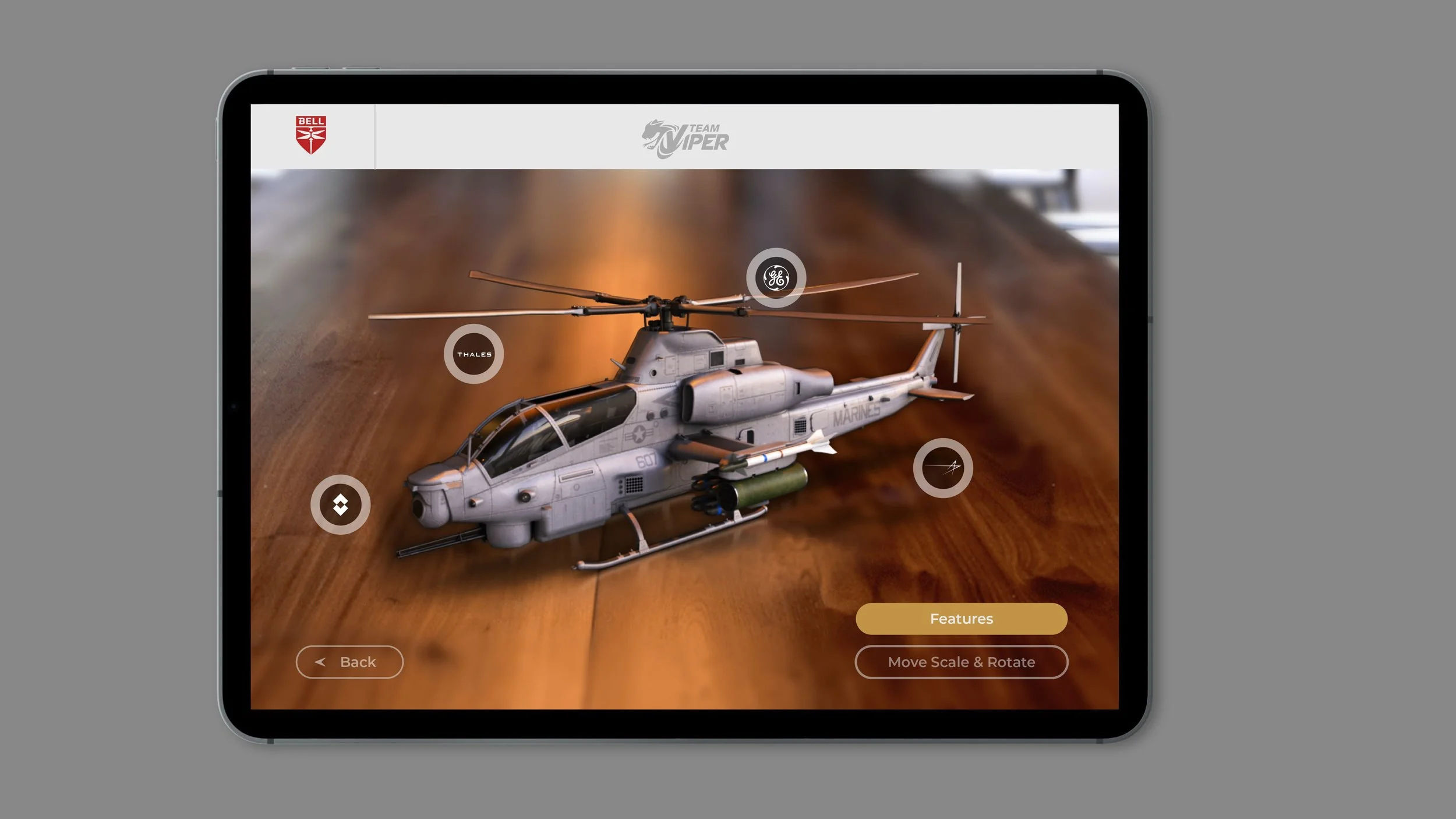 A tablet screen displaying a 3D model of a military helicopter with labels from GE, Thales, and others, on a wooden surface background.