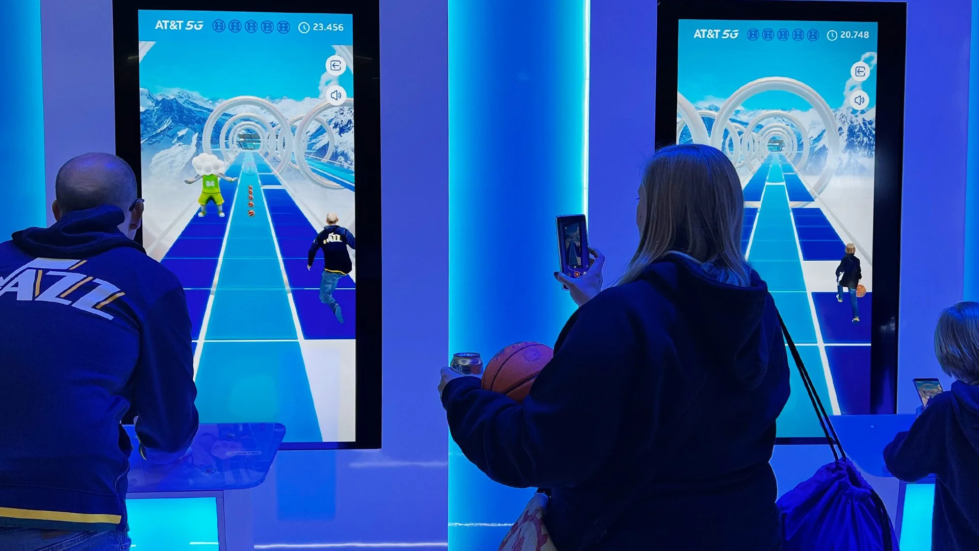 People playing a virtual reality snowboarding game at an indoor arcade, with screens displaying snowy mountain scenes and animated characters.