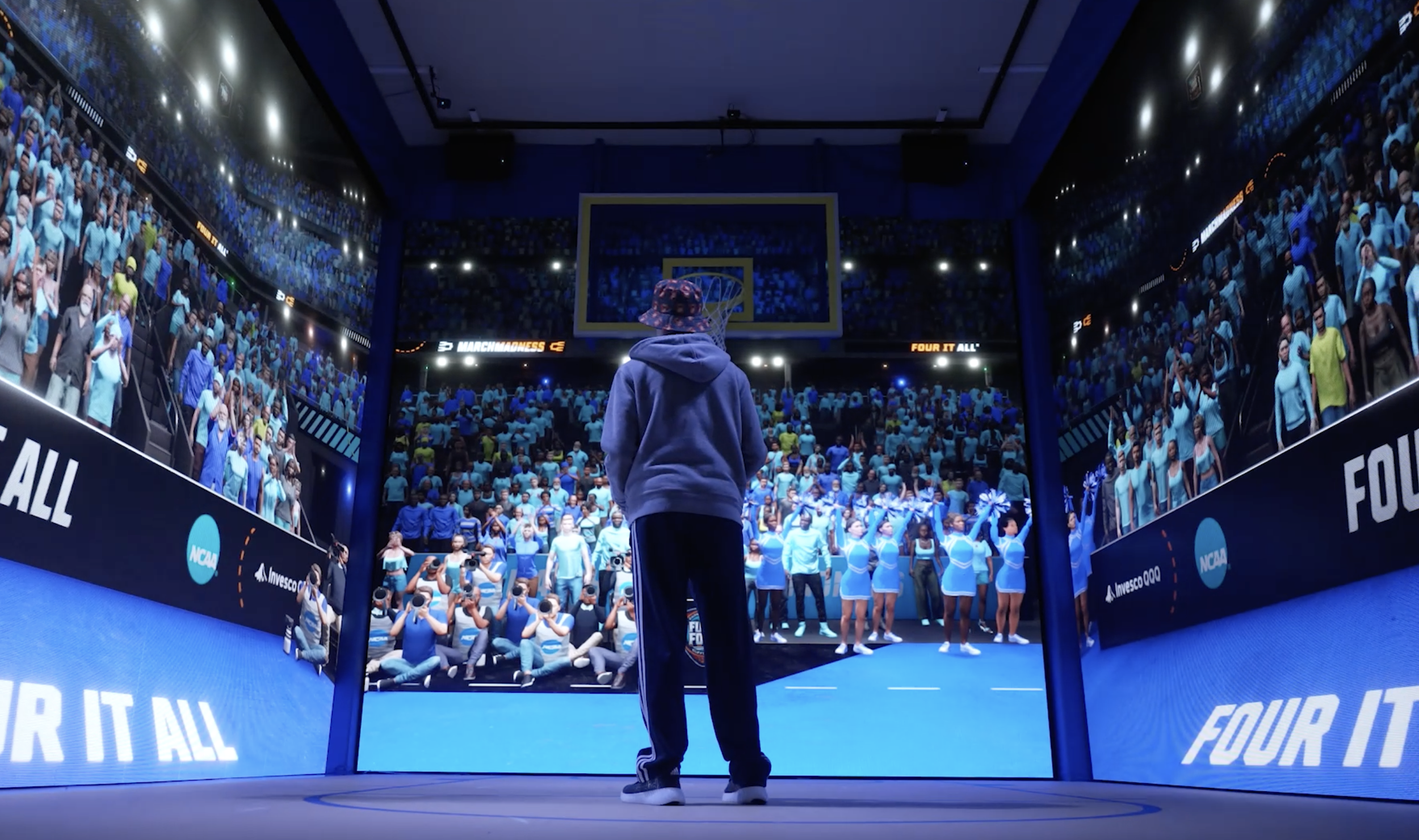 A person standing on a stage in front of a large screen displaying a packed audience at the NCAA March Madness event.