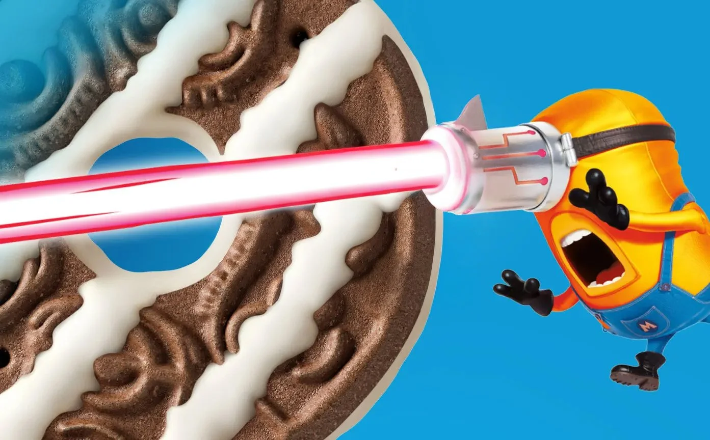 Animated Minion character shooting a laser from a machine gun attached to its head at a pile of Oreo cookies.