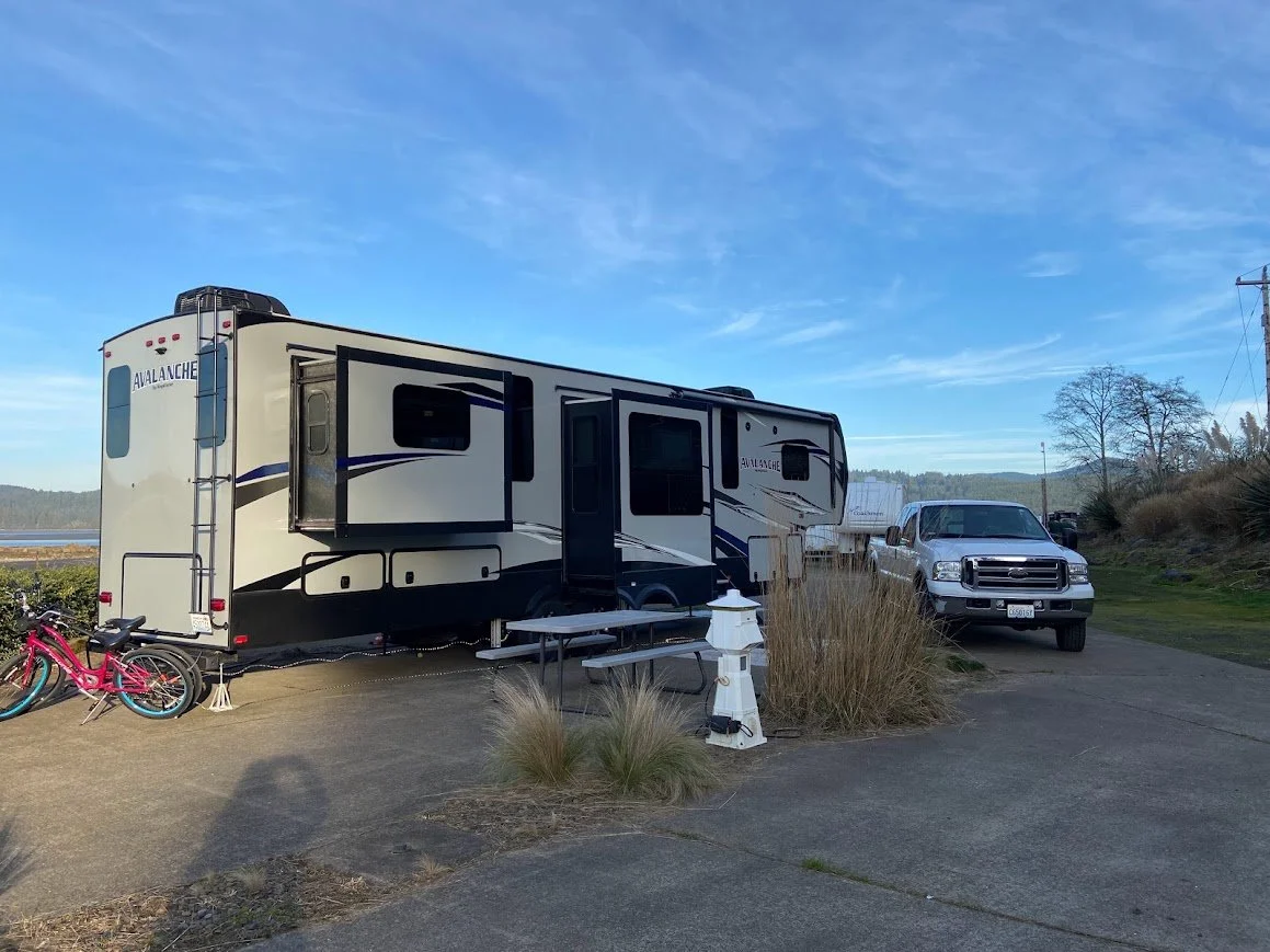 5th wheel with truck and bike at a campsite near water