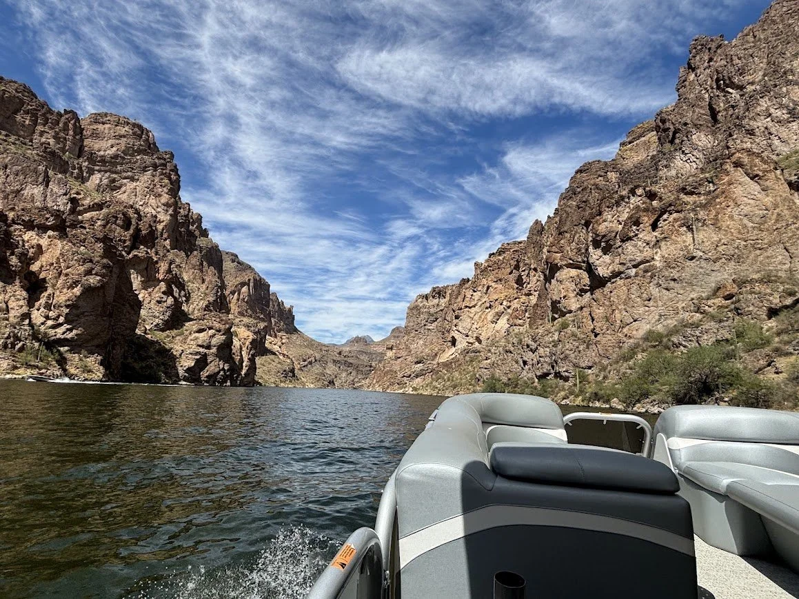 A boat on a lake surrounded by tall, rugged canyon walls under a partly cloudy sky.
