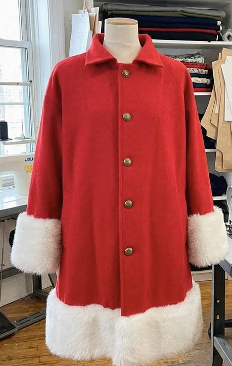 Red coat with white fur cuffs and hem displayed on a mannequin in a sewing or fabric store.