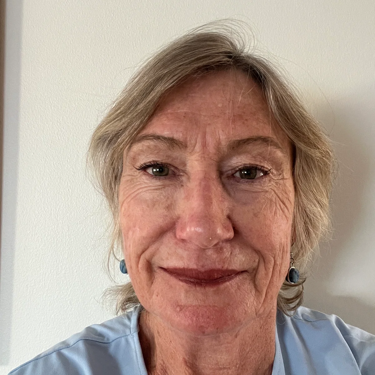 A smiling woman with short blonde hair, and blue top.