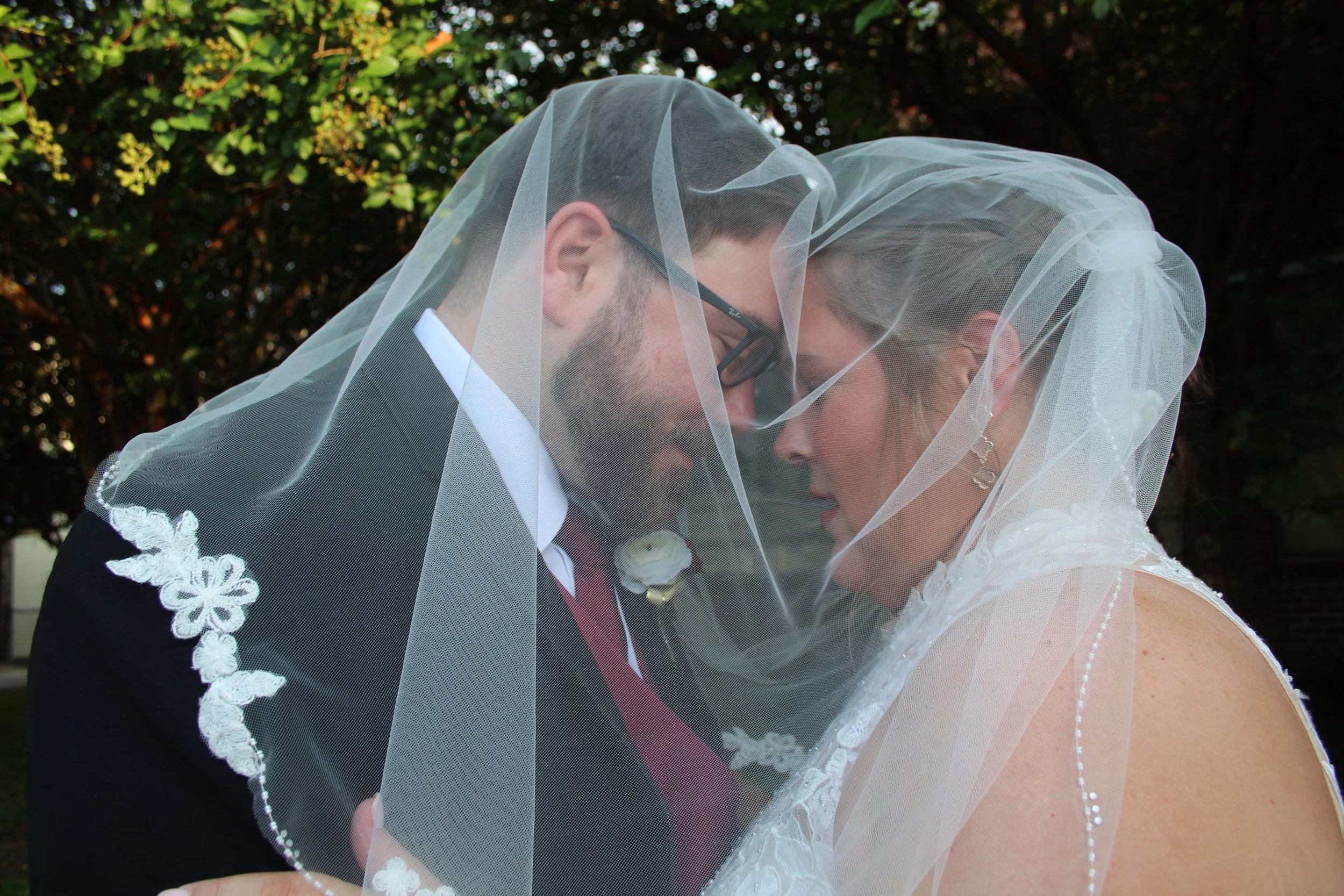 A bride and groom sharing a romantic dance outdoors during sunset, with silhouettes and trees in the background.