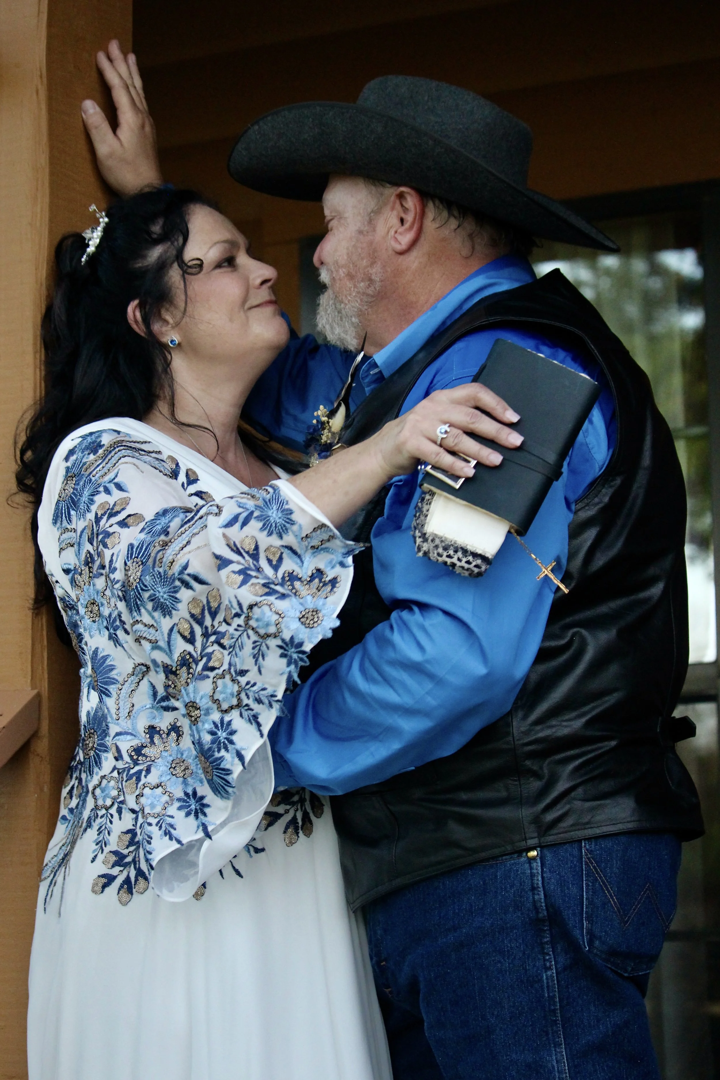 A couple dressed in formal attire holding hands outdoors, with trees and decorative barrels in the background.