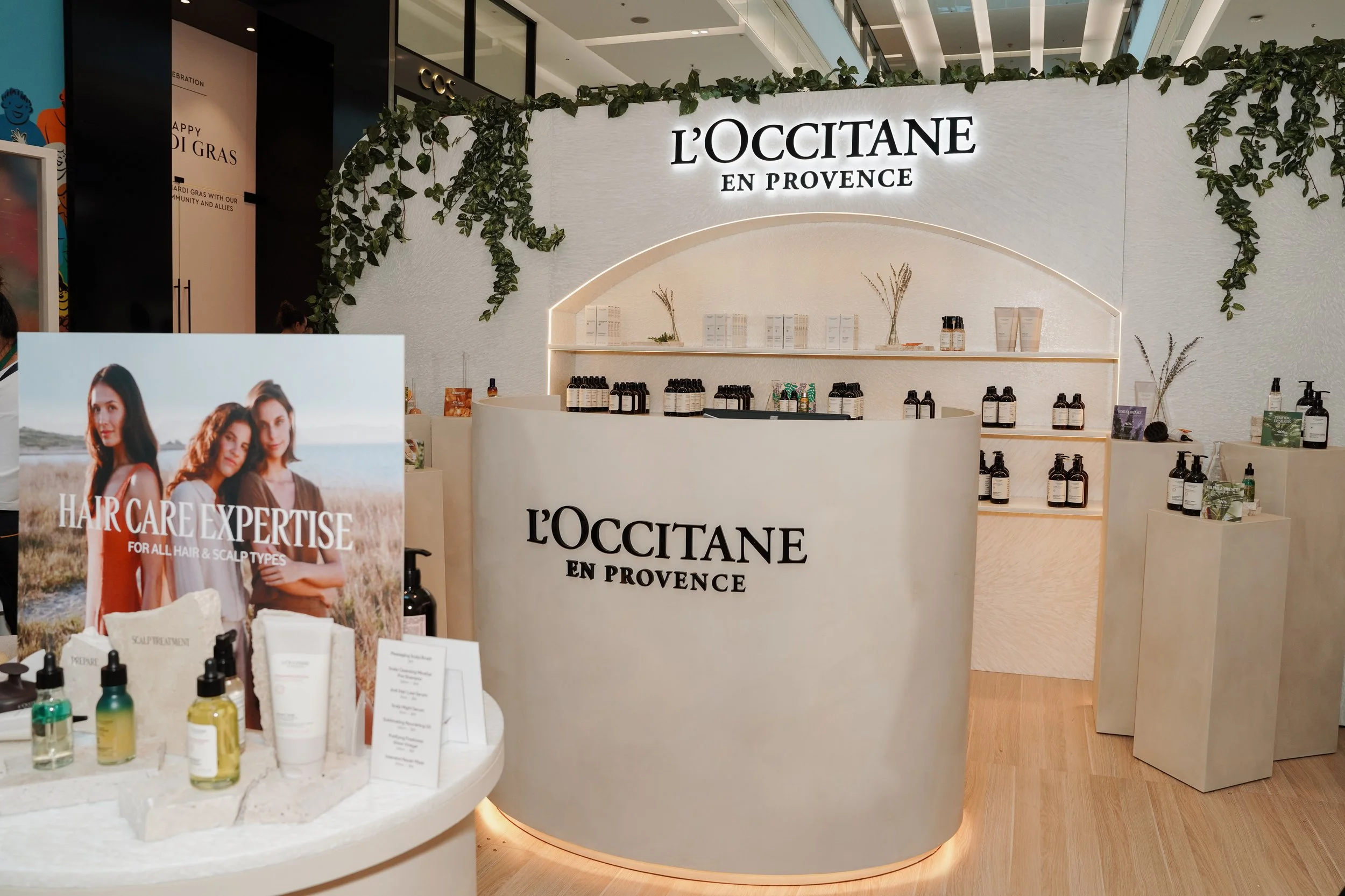 L'Occitane en Provence kiosk display at a shopping mall, showcasing skincare and hair care products on shelves and promotional signage.