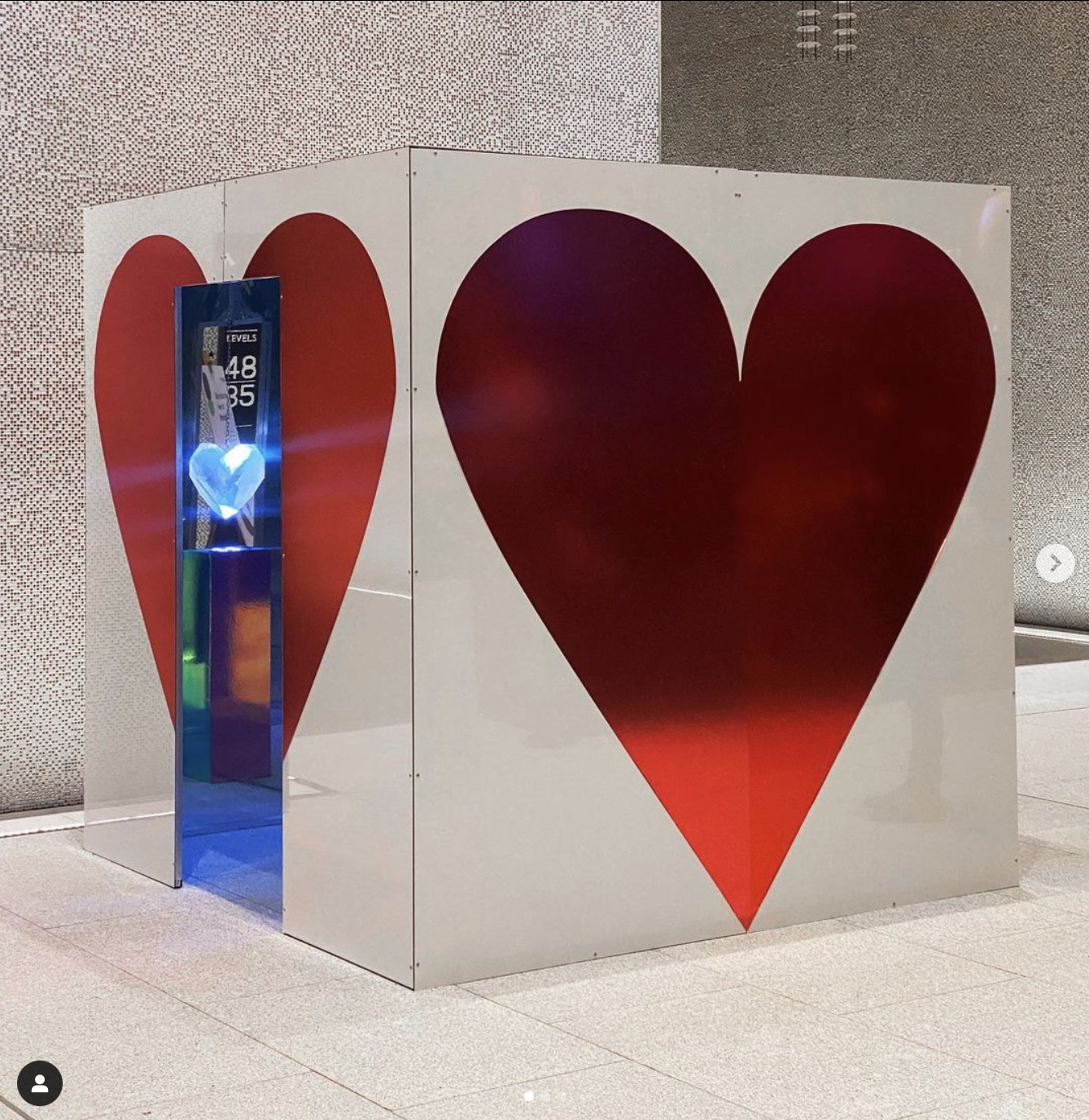 A decorated installation with two large red hearts on a white background, featuring a heart-shaped design on the front. There is a small illuminated display inside the left heart. Vivid Sydney Heart of Barangaroo JLL International Towers