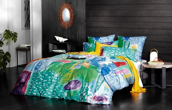 Colorful abstract patterned bedding with pillows on a modern bed in a dark wood paneled bedroom. Ken Done for Sheridan
