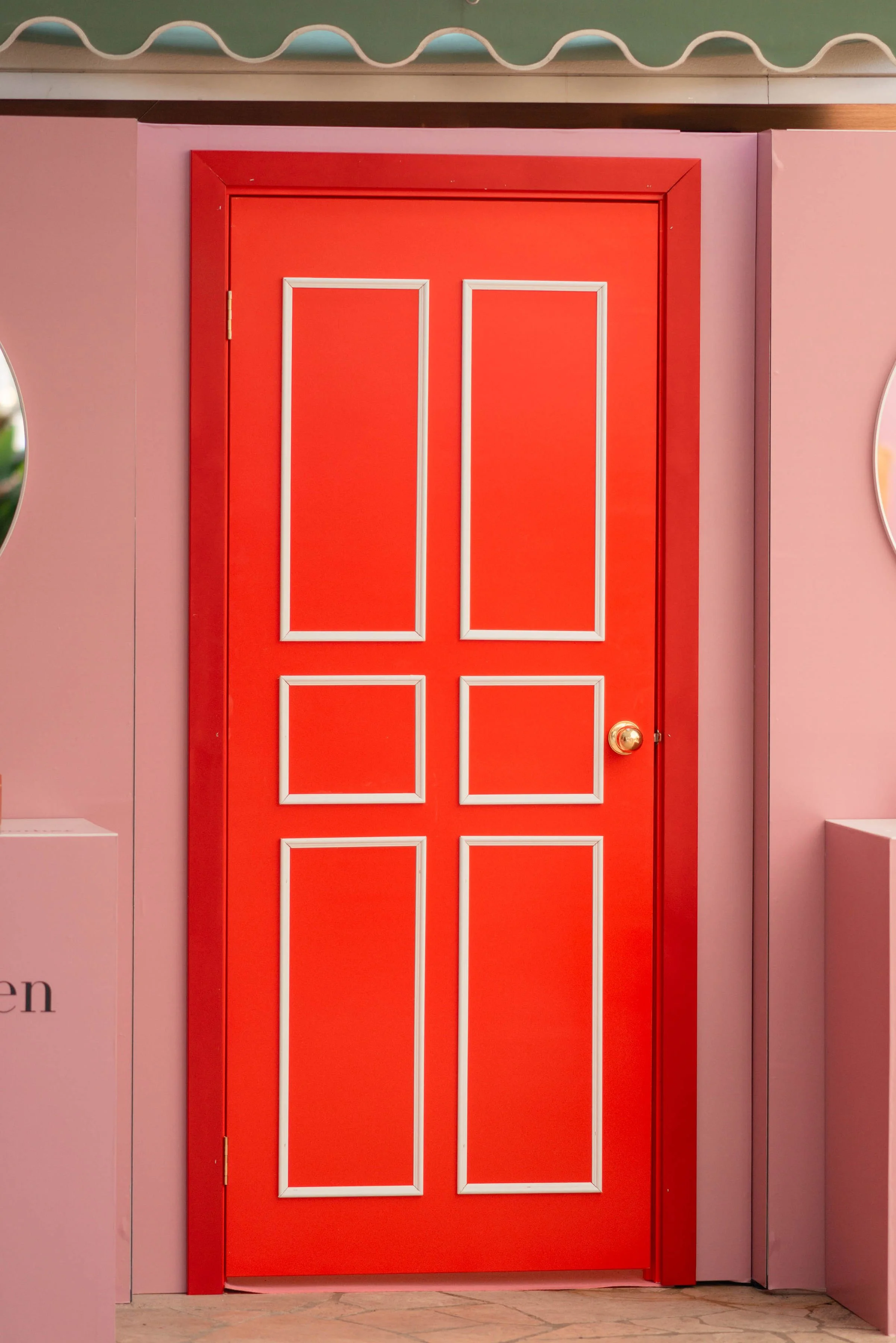 Bright red door with white trim panels, gold doorknob, set in pink wall, with decorative wall design above. Elizabeth Arden