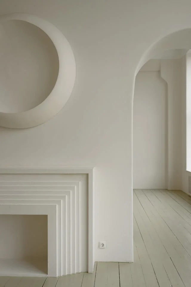 Minimalist white interior wall with a circular cutout and a modern, stepped fireplace design.