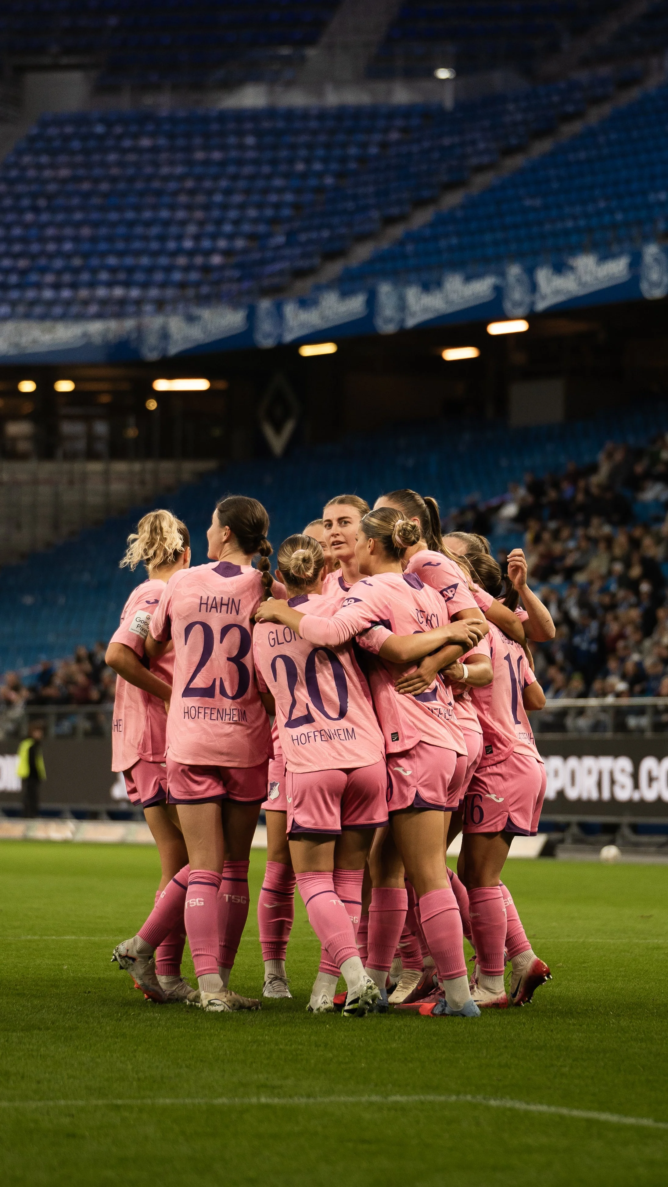 Fußballspielerinnen in pinken Trikots leicht umarmend und jubelnd auf dem Spielfeld.