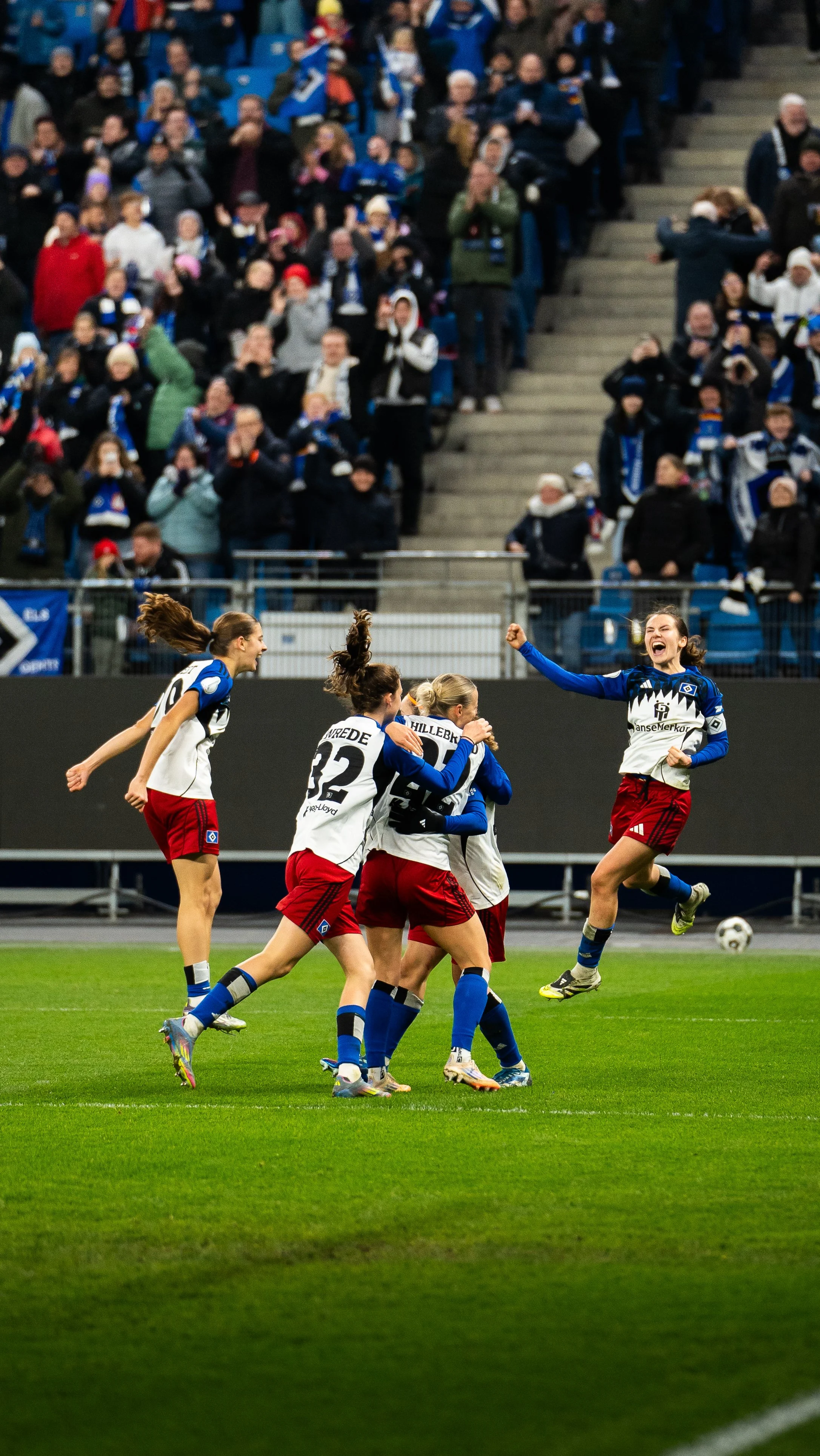 Fußballspielerinnen feiern auf dem Spielfeld, während das Publikum im Hintergrund zuschaut.