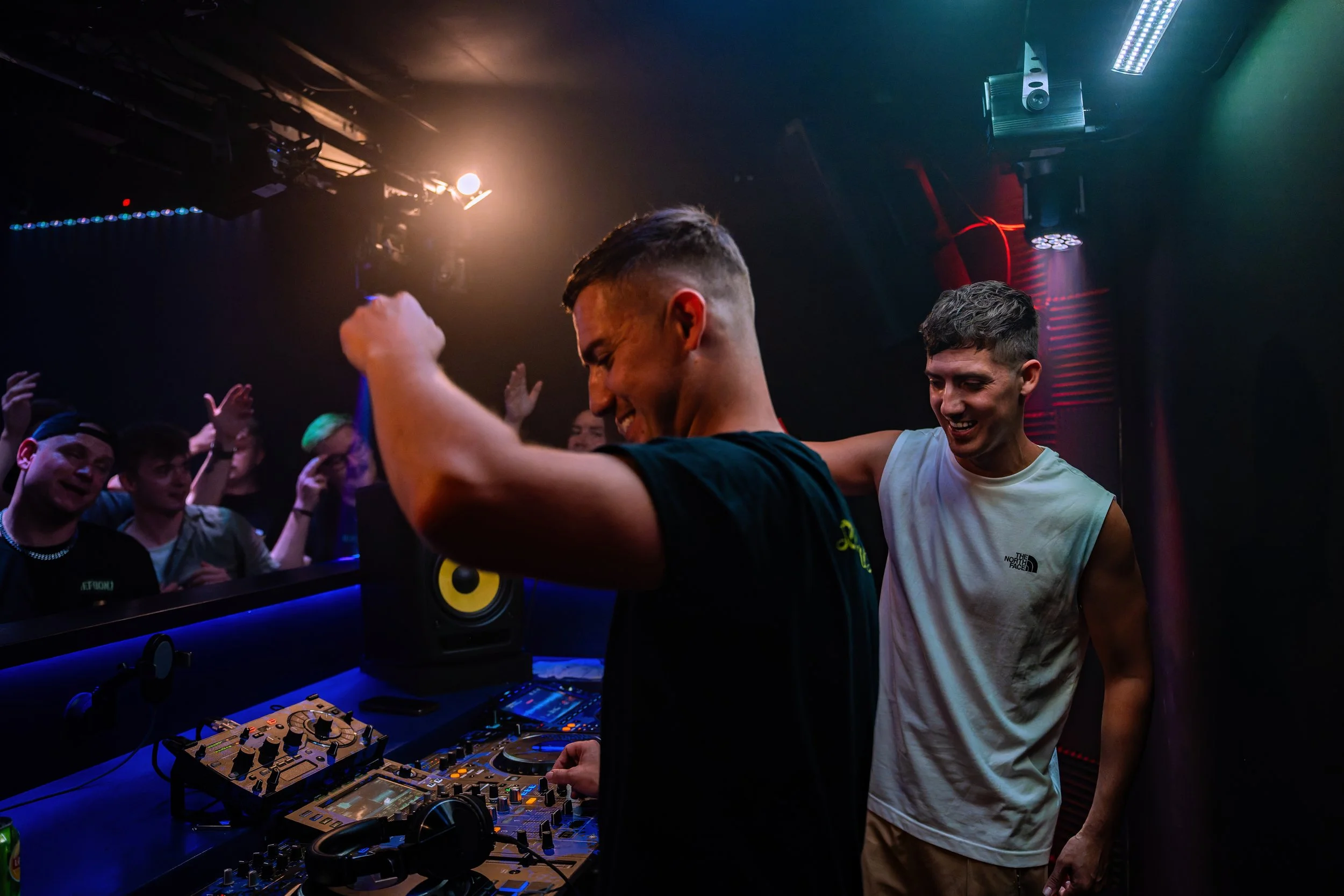 DJ spielt Musik in einem Club, während eine Gruppe von Freunden vor ihm tanzt und Spaß hat.