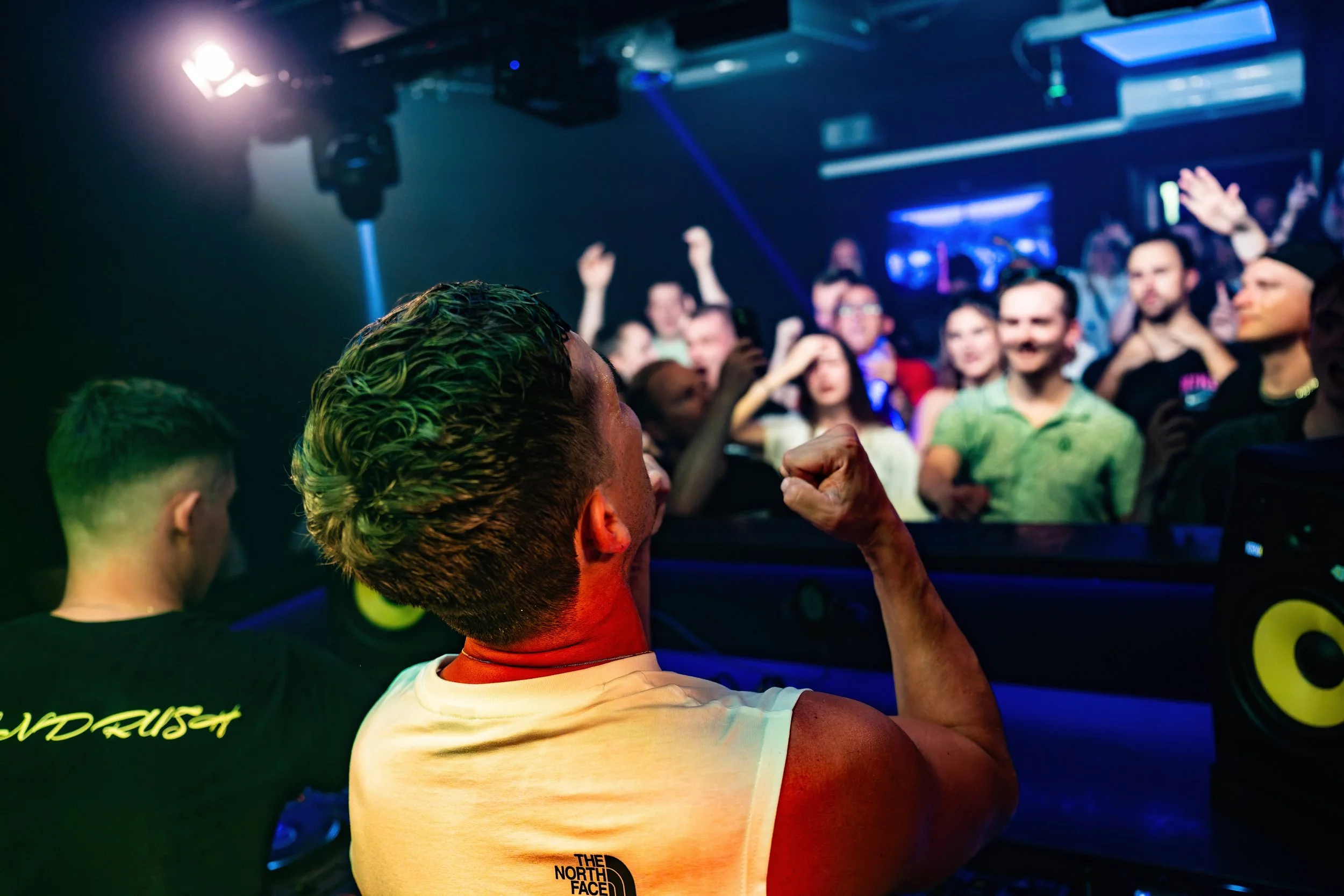 DJ mit Hand in Fäuste bei einem Clubabend, begeistertes Publikum im Hintergrund bei Tanz und Feierlichkeiten.