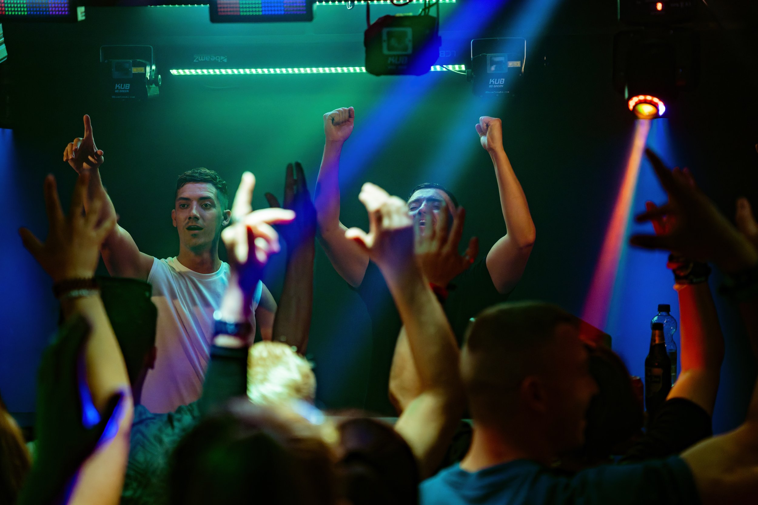 Tanzende Menschen in einer Diskothek mit buntem Bühnenlicht, einige mit erhobenen Armen und gestikulierend, bei einer Party
