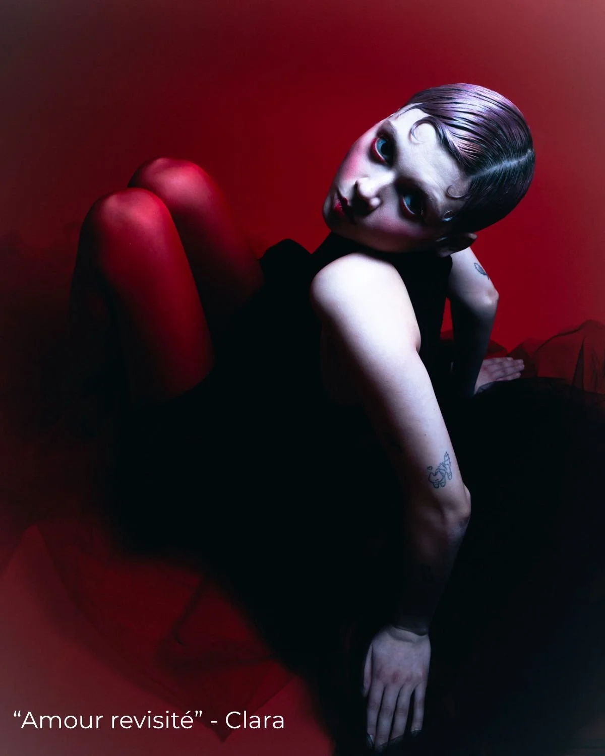 Une femme aux cheveux courts et maquillage remarquable posant sur un fond rouge, vêtue d'une robe noire.