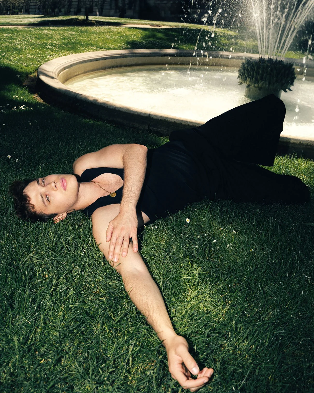 Une personne allongée sur l'herbe devant une fontaine.