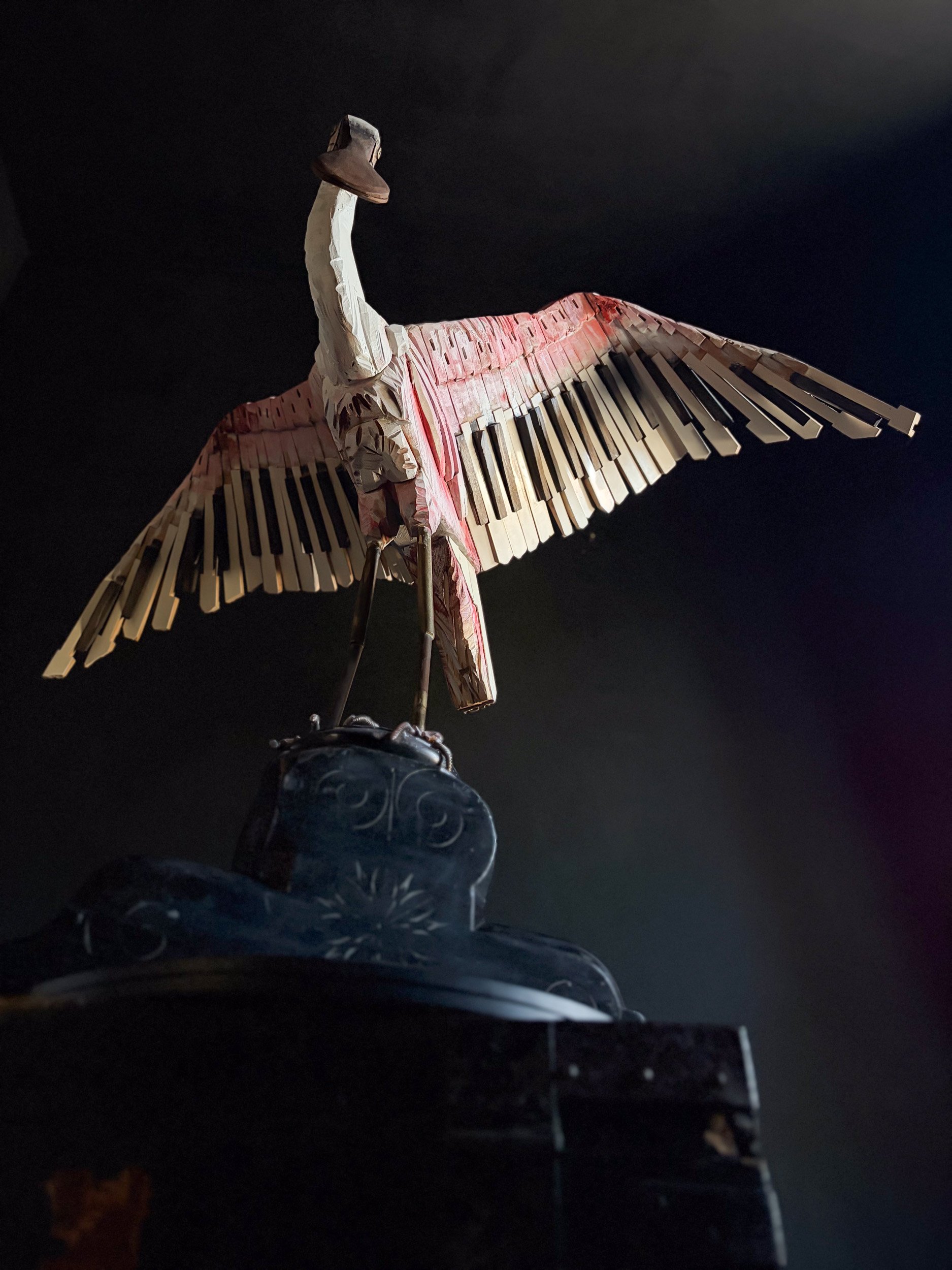 Roseate Spoonbill sculpture made from piano parts shown from underneath on black background.