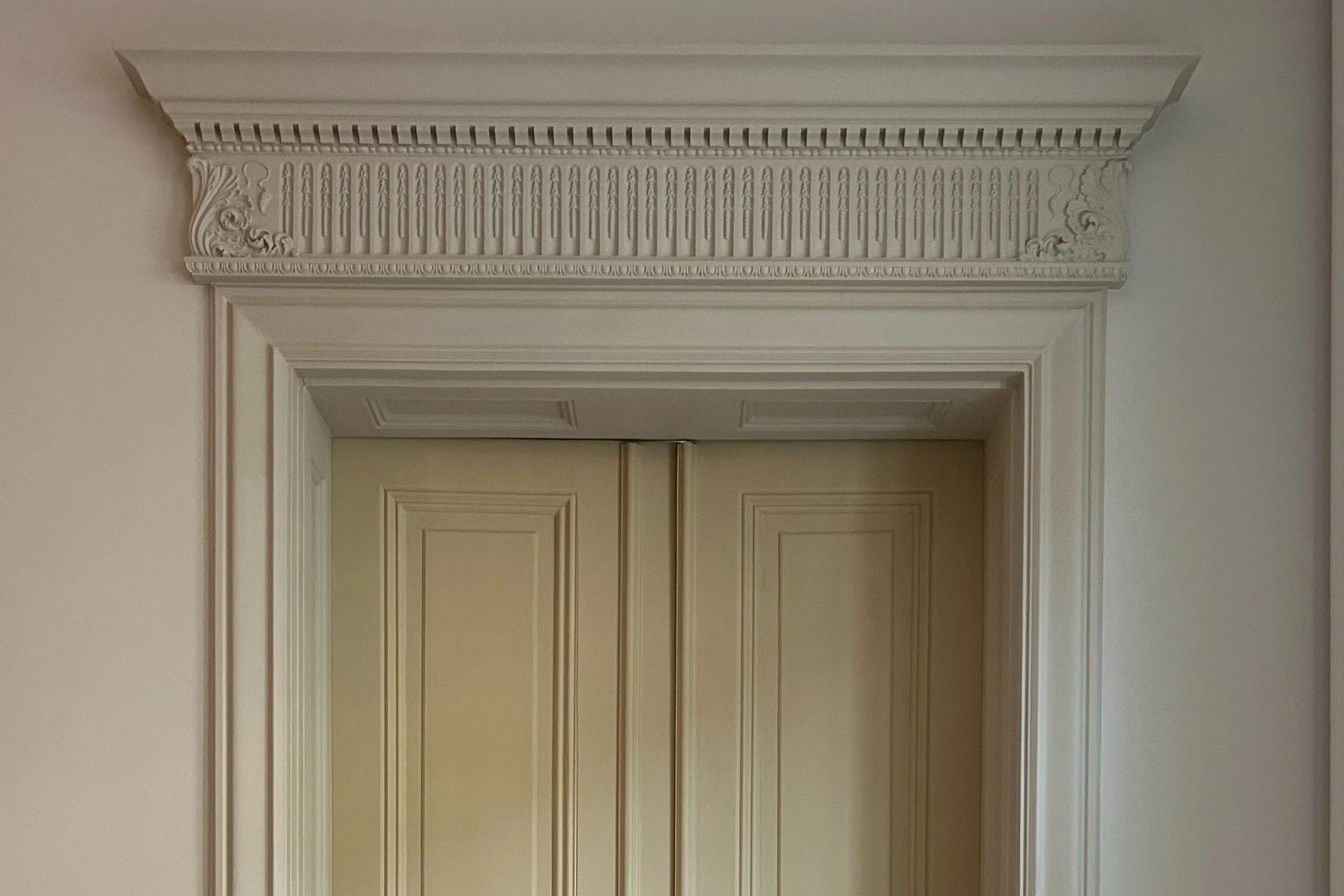 Det är ett dekorativt vitt träfönsteromramning med detaljerad karvad carving.