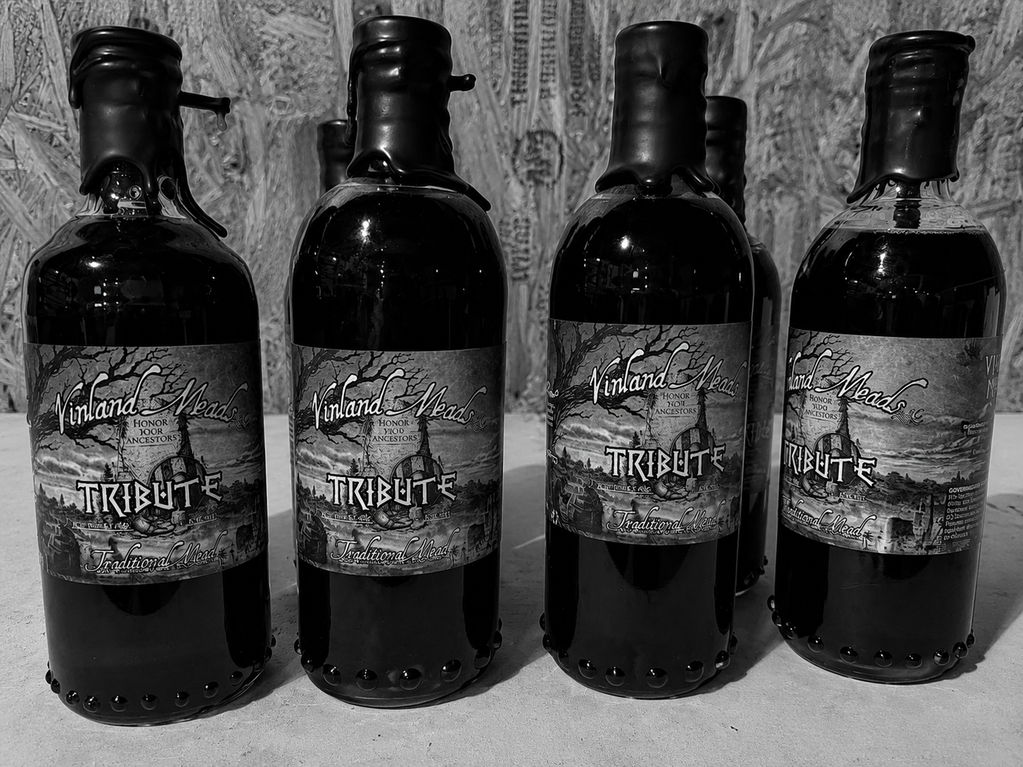 Four dark glass bottles with labels that read Vinland Meads Tribute Traditional Mead, arranged in a row on a surface with a textured background.
