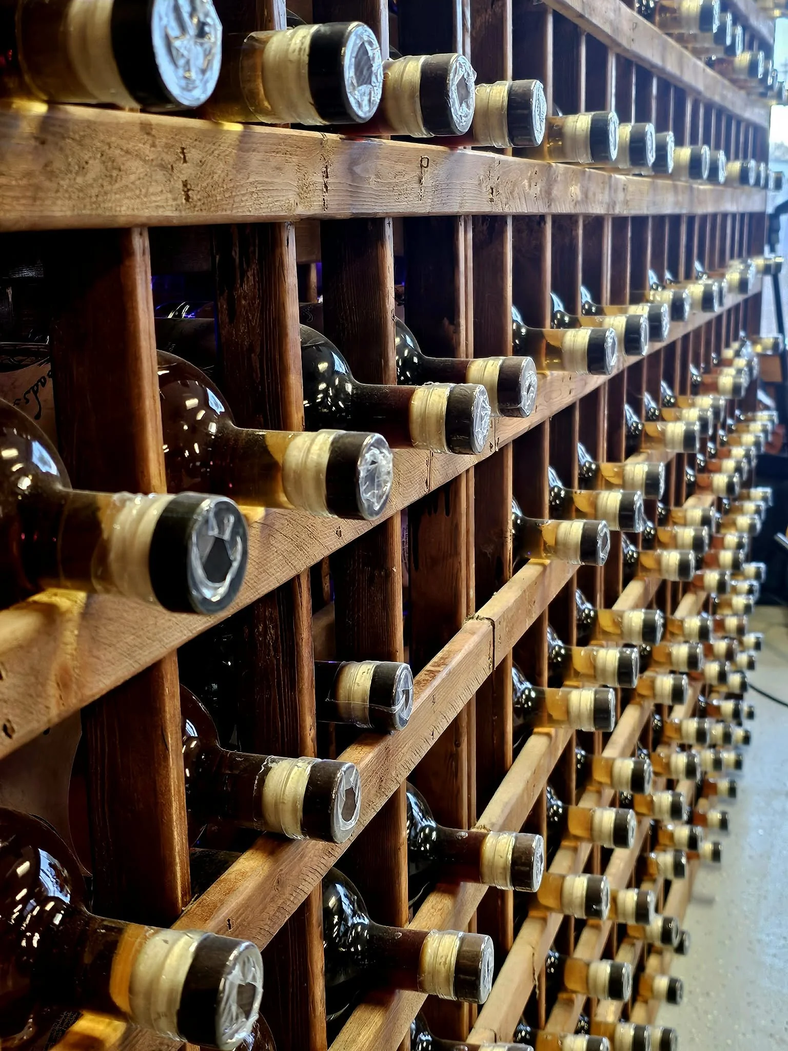 A wooden wine rack holding multiple bottles of wine lying horizontally with their necks facing inward.
