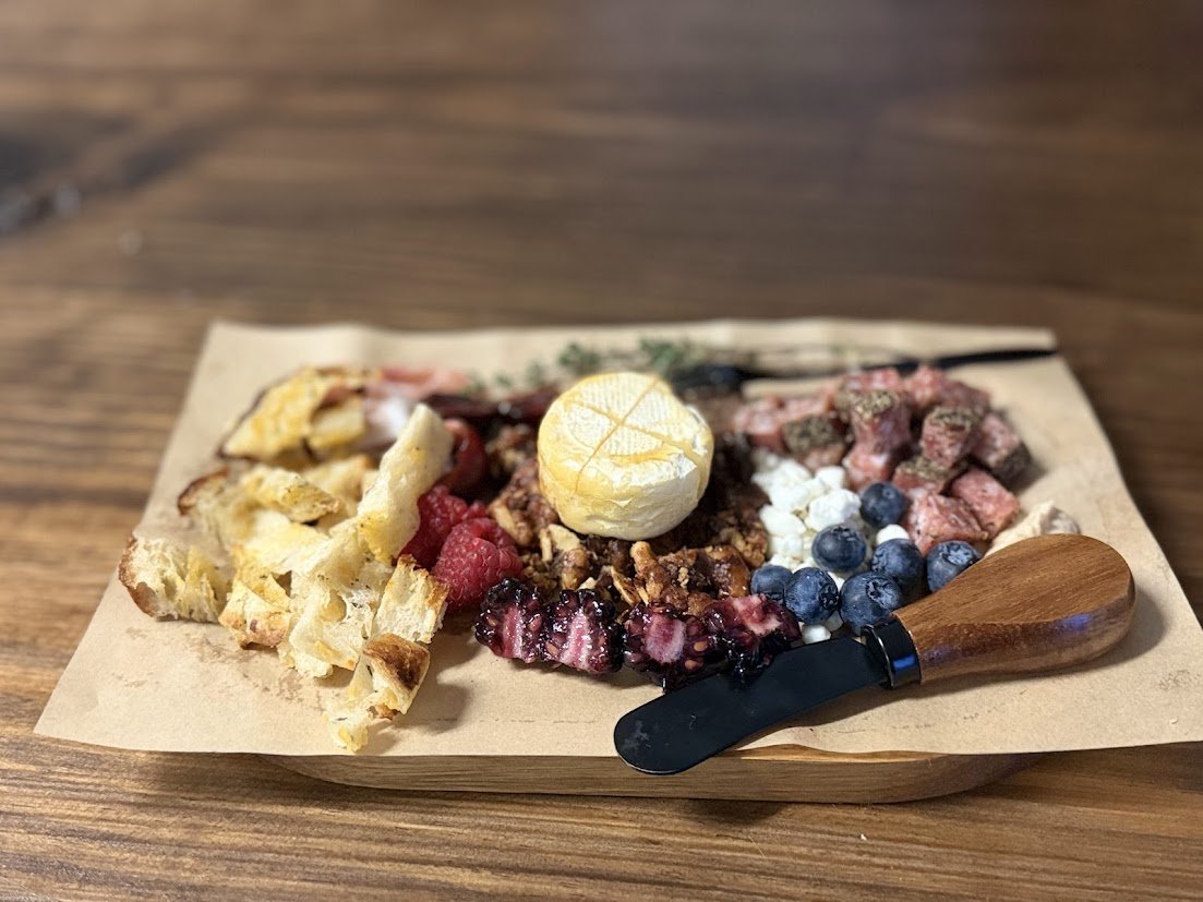 Assorted dessert with crust, berries, whipped cream, and a small round dessert on a paper-lined tray with a wooden spoon.
