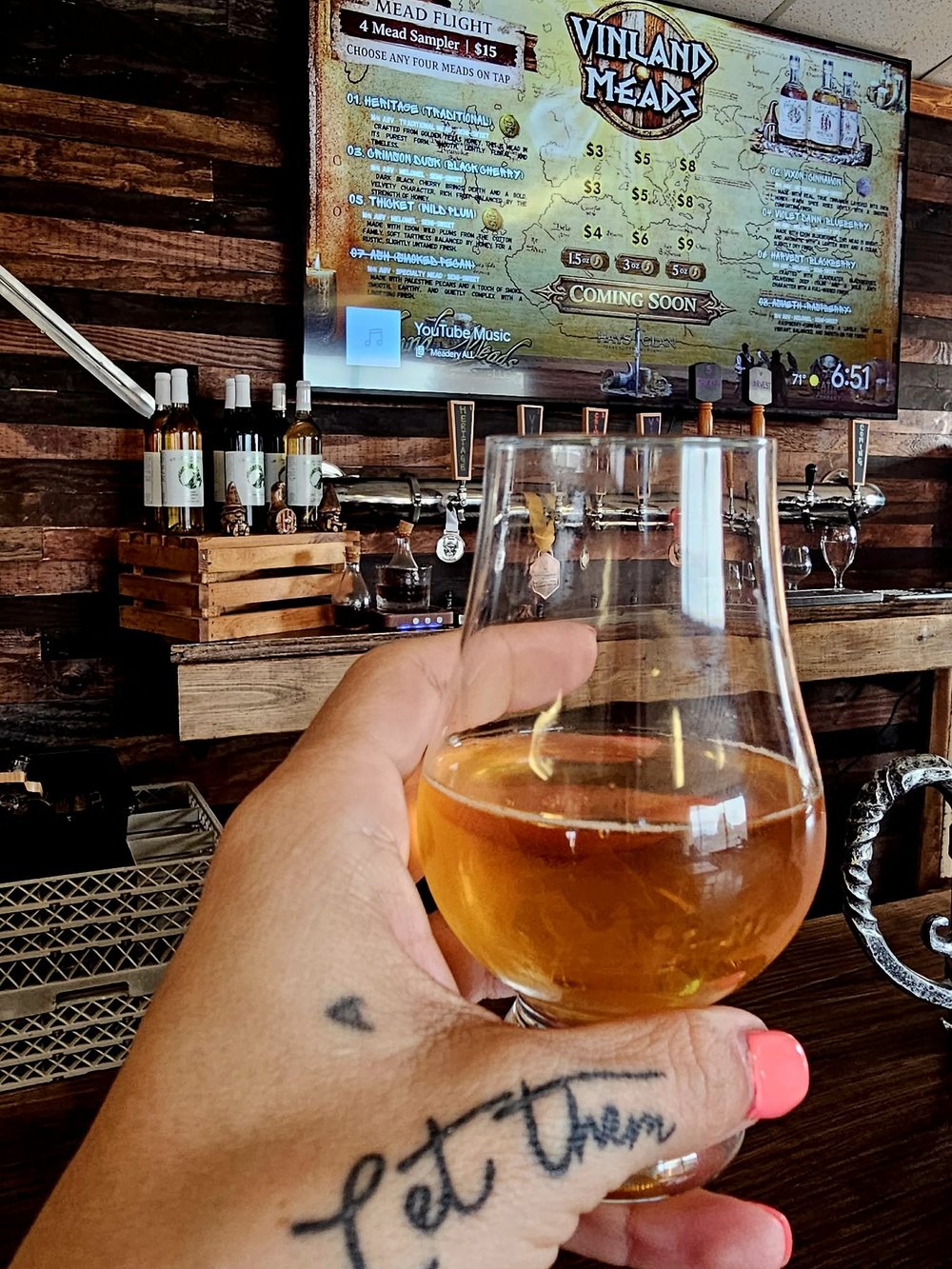 A glass of golden mead held in front of the wooden bar at the Vinland Mead Hall.