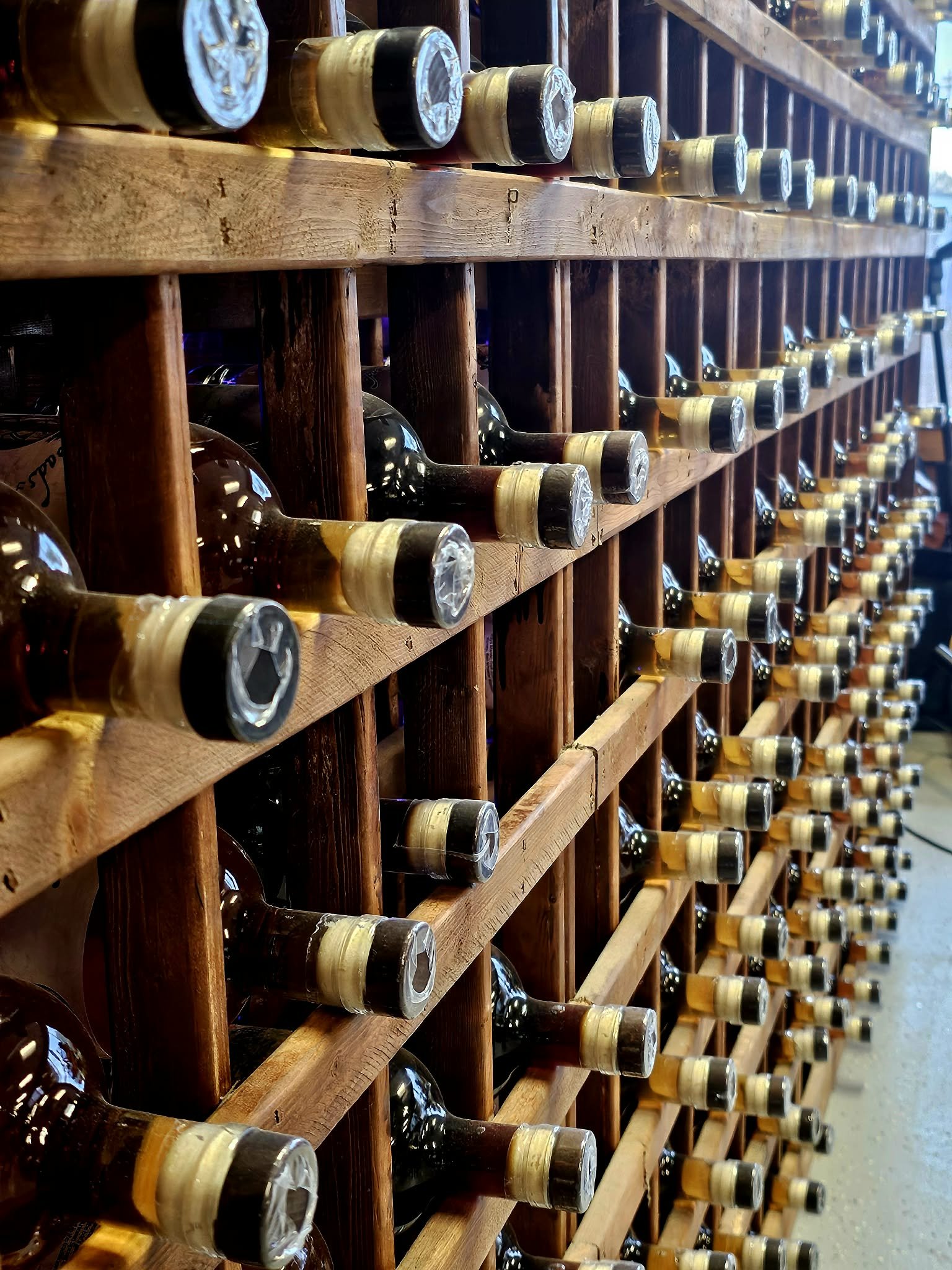 Display of multiple bottles of wine stored horizontally in wooden racks.