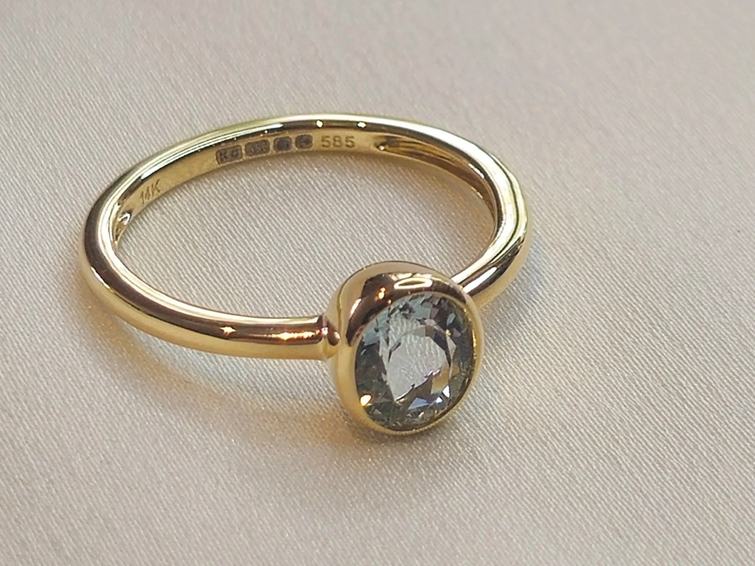 Gold ring with a large aquamarine gemstone, resting on a light-colored fabric surface.