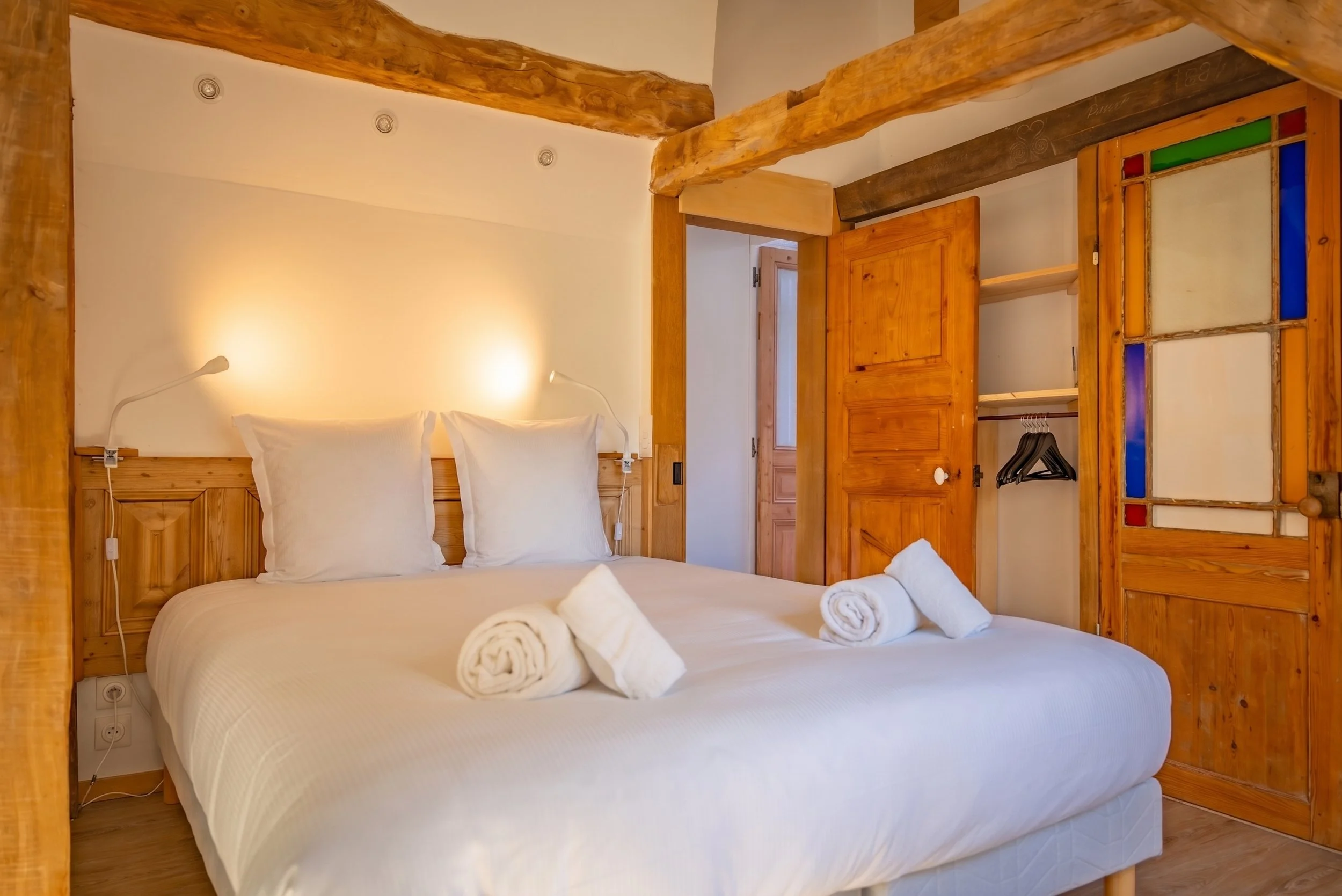 Chambre avec lit double, tête de lit en bois, éclairage intégré, porte ouverte vers une salle de bain avec vasque en bois.