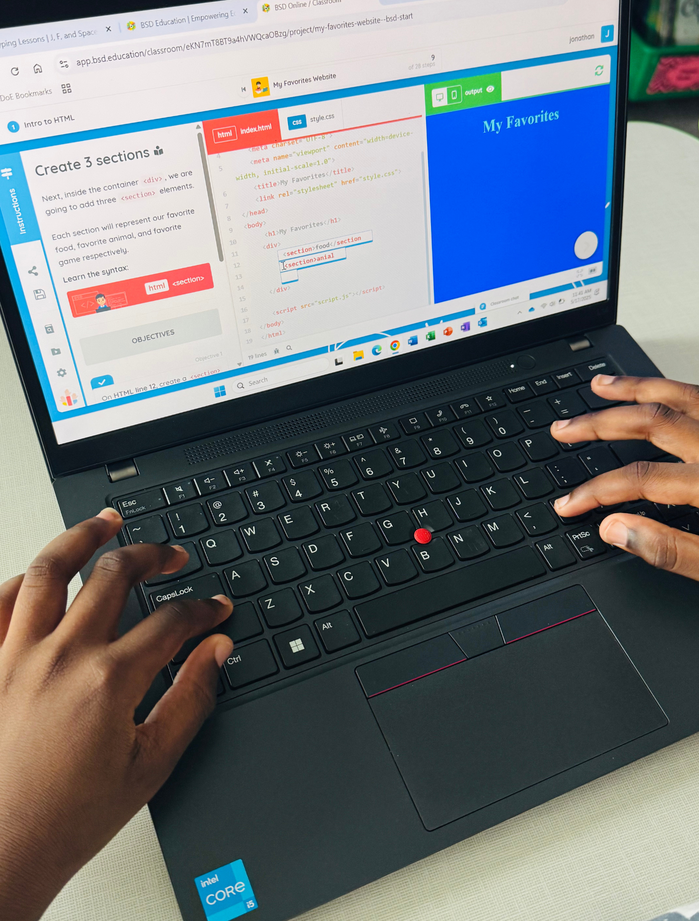 Hands typing on a black laptop keyboard with code and a webpage on the screen, showing HTML and CSS elements, and a blue section titled 'My Favorites'.