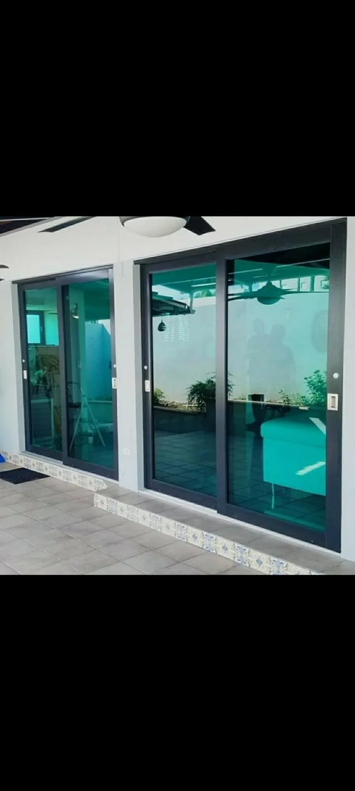 Sliding glass doors leading to an outdoor patio with tiled flooring and plants inside reflected in the glass.