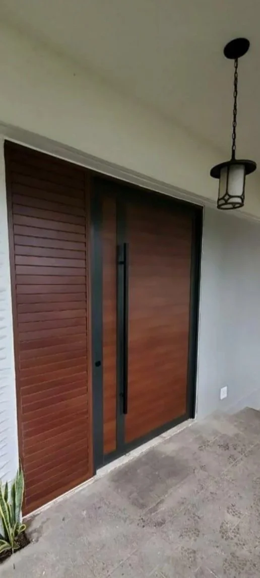 Front door with wooden panels, black handle, and sliding screen door, under a hanging lantern-style porch light, with a potted plant visible in the corner.