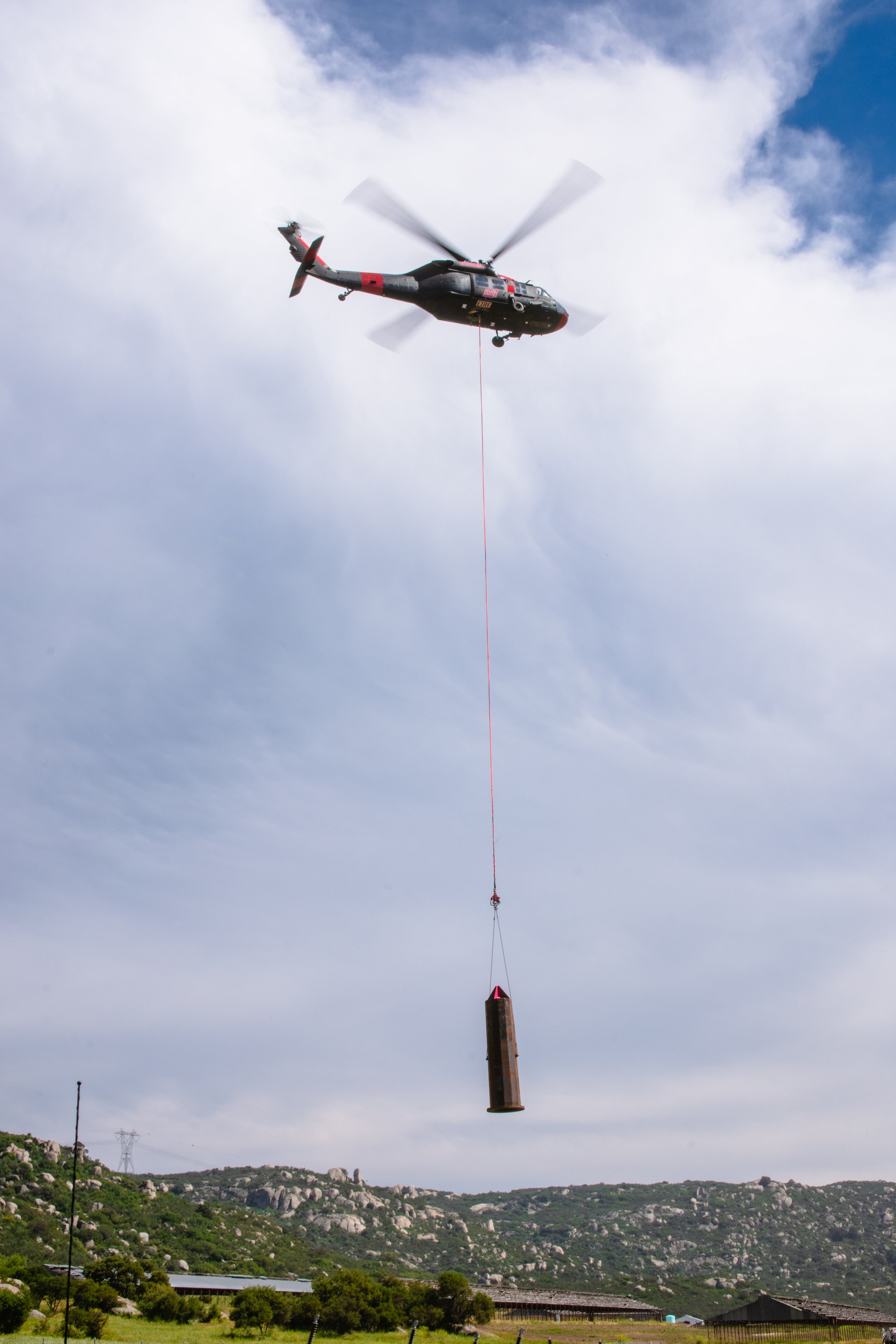 Helicopter flying over mountains with a long line and pole