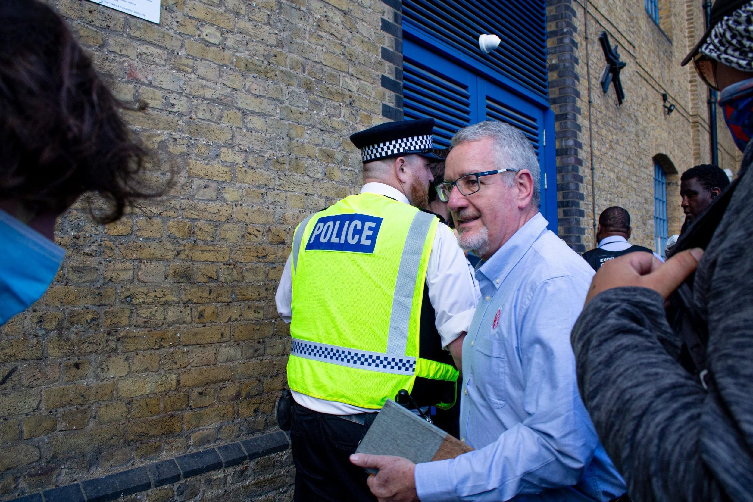 An attendee of the DSEI Arms fair weaves through the crowd of protestors and police in order to attend the event through a side door, 2025.