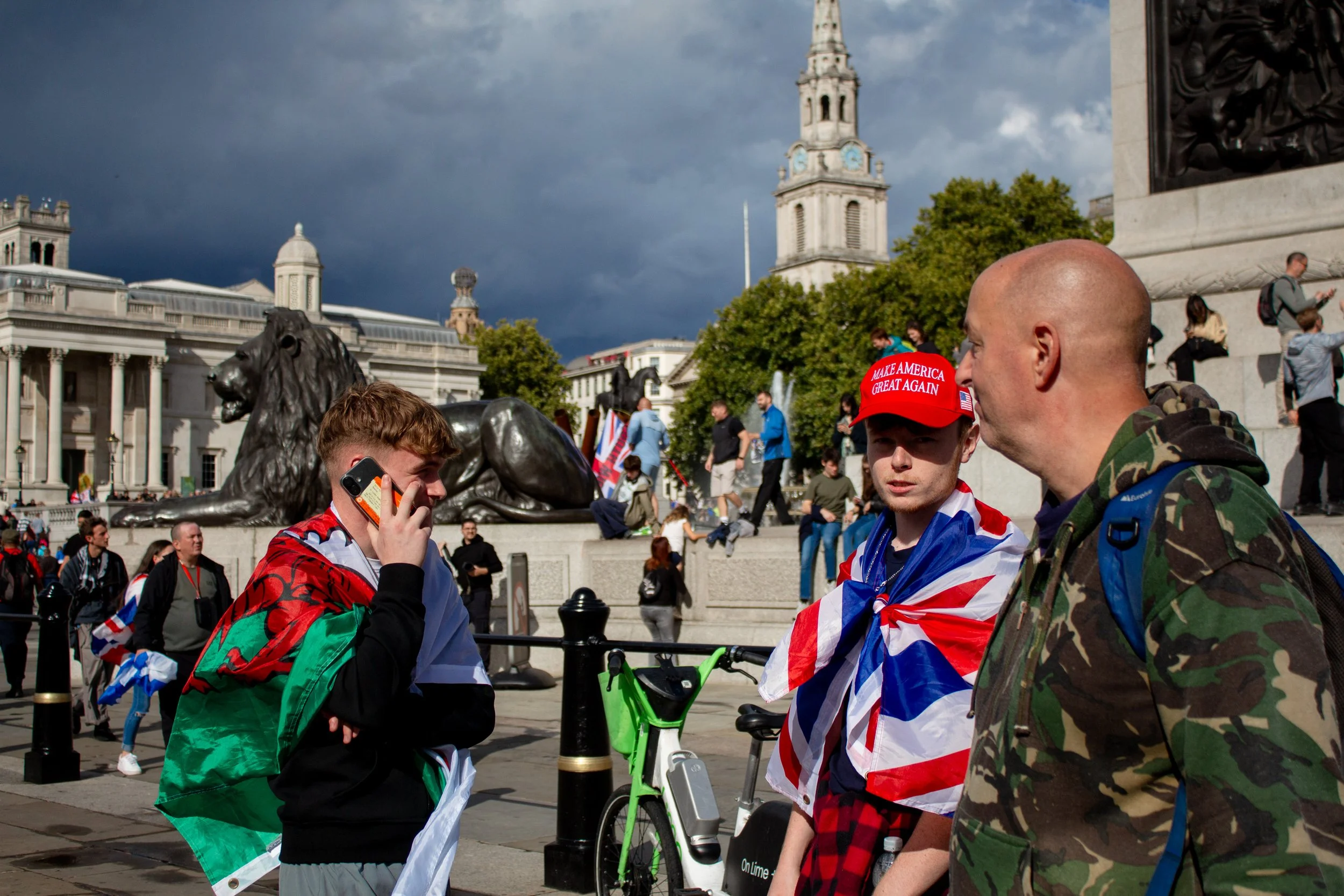 A boy wearing a 'Make America Great Again' hat stands by Trafalgar Square Monument.