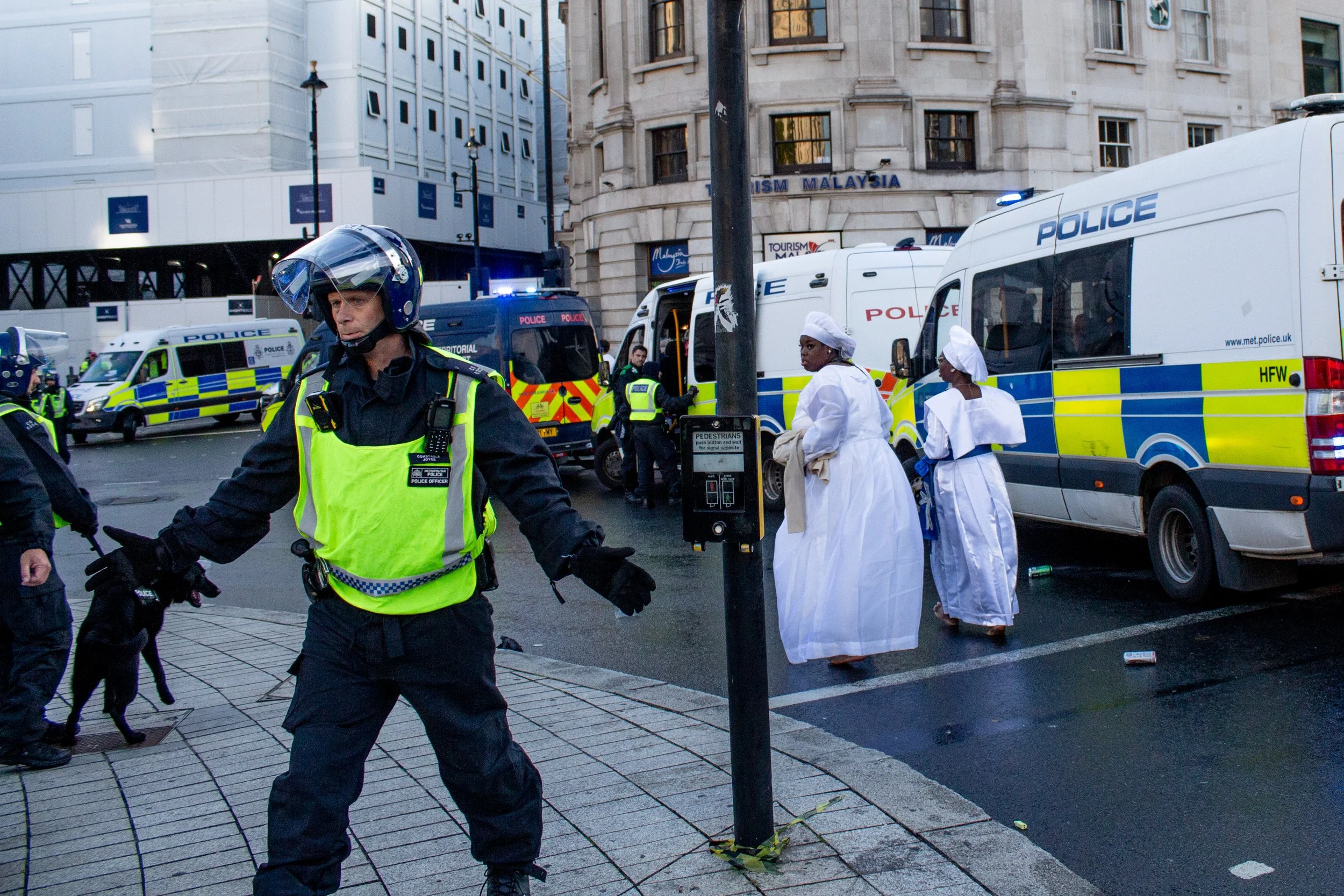 Two ladies hurry across Trafalgar Square while a policeman prevents interference.