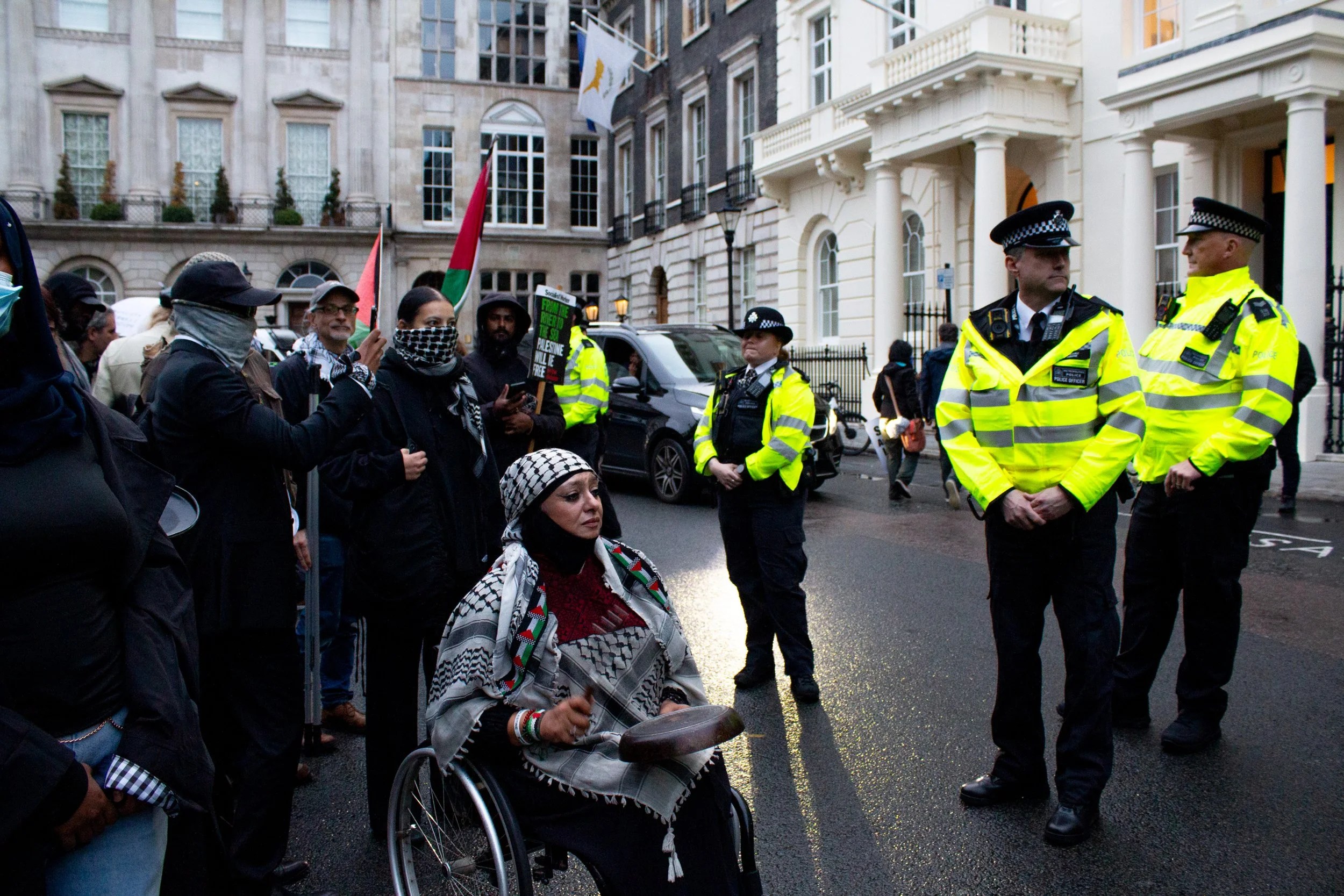 A protestor outside Chatham House hits a kitchen utensil against a pan, symbolising the ongoing man-made famine in Gaza, 2025.