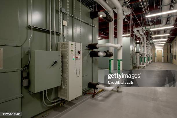 Industrial facility with pipes, control panels, and machinery in a corridor.